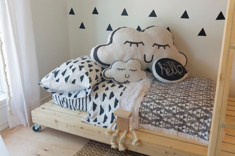 This gender neutral kids room features bright white walls, simple modern decor and custom made wooden beds. The bottom bed even has wheels on it so that it can be moved around when needed.