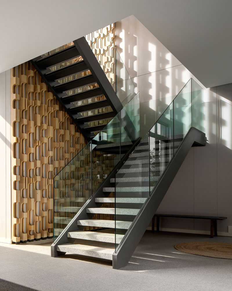 These modern stairs with a glass railing, rise alongside a CNC-cut timber screen. #CNC #TimberScreen #Stairs #ModernStairs #GlassRailing