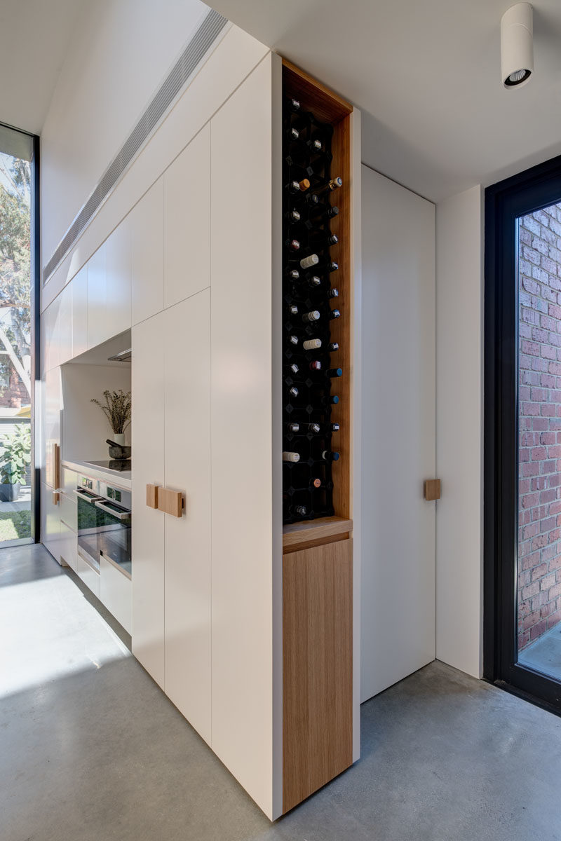 Kitchen Ideas - This modern kitchen has a large wood peninsula, minimalist white cabinets, oversized hardware, and built-in wine storage. Behind the kitchen is a door that leads to the laundry room. #KitchenIdeas #ModernKitchen #KitchenDesign