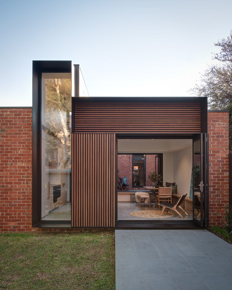 The view from the yard of this modern house addition, showcases the new brickwork that used recycled bricks to tie in with the original house, wood accents, and the deep steel frames. #HouseAddition #Architecture #ModernHouse