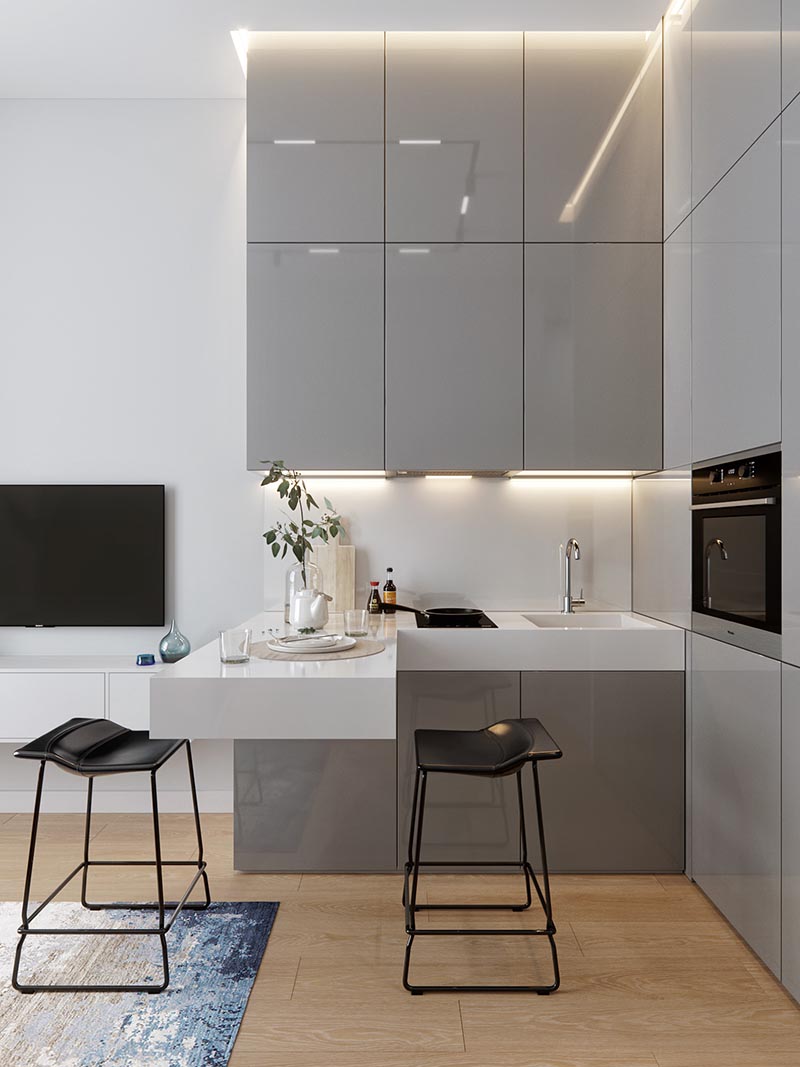 A small kitchen with an L-shaped countertop, integrated fridge, minimalist grey cabinets, hidden lighting, and a cantilevered peninsula for dining. #SmallKitchen #TinyKitchen #KitchenDesign #KitchenLayout