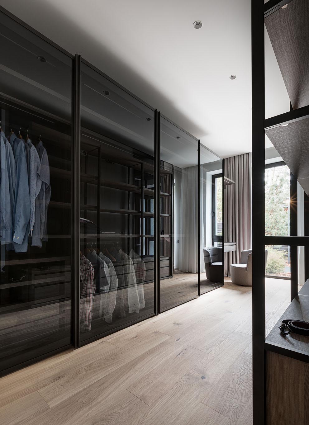 A modern walk-through closet includes black glass doors.