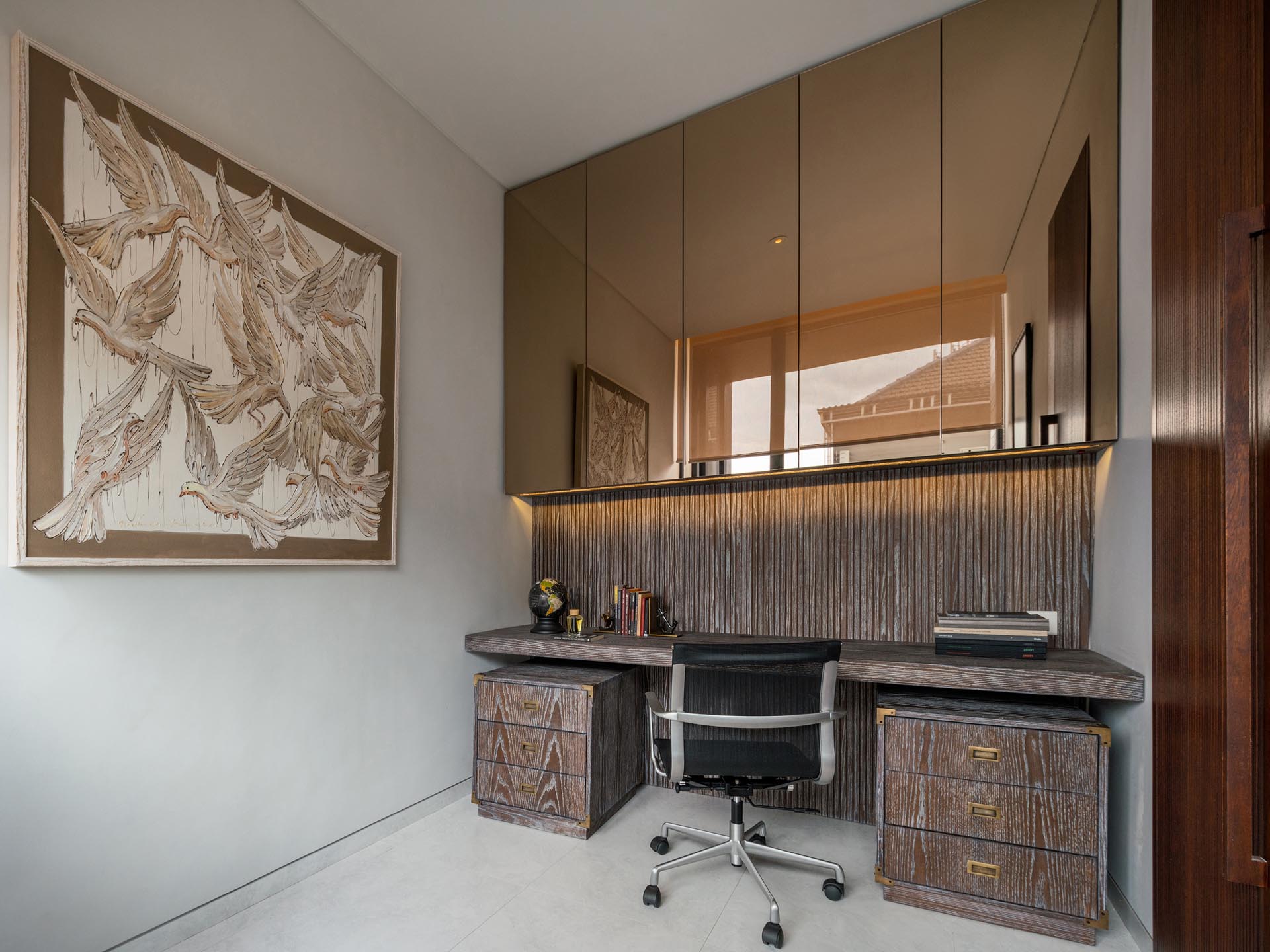 A home office has mirrored cabinets positioned above the desk.