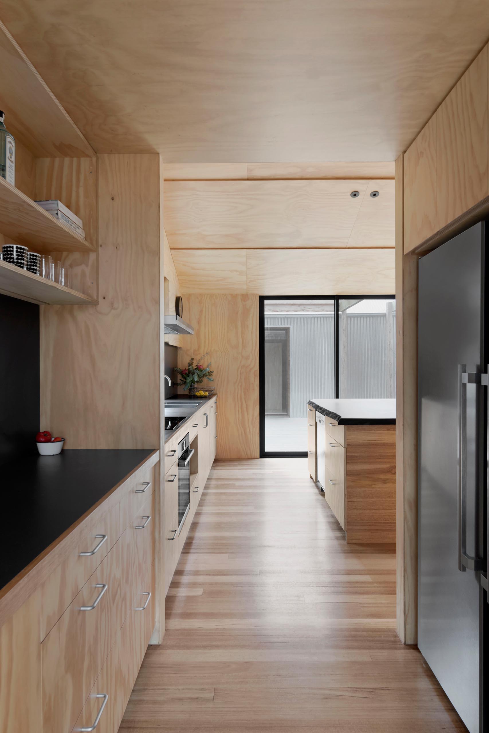 A modern plywood kitchen with a matte black countertop and backsplash, and separate pantry.