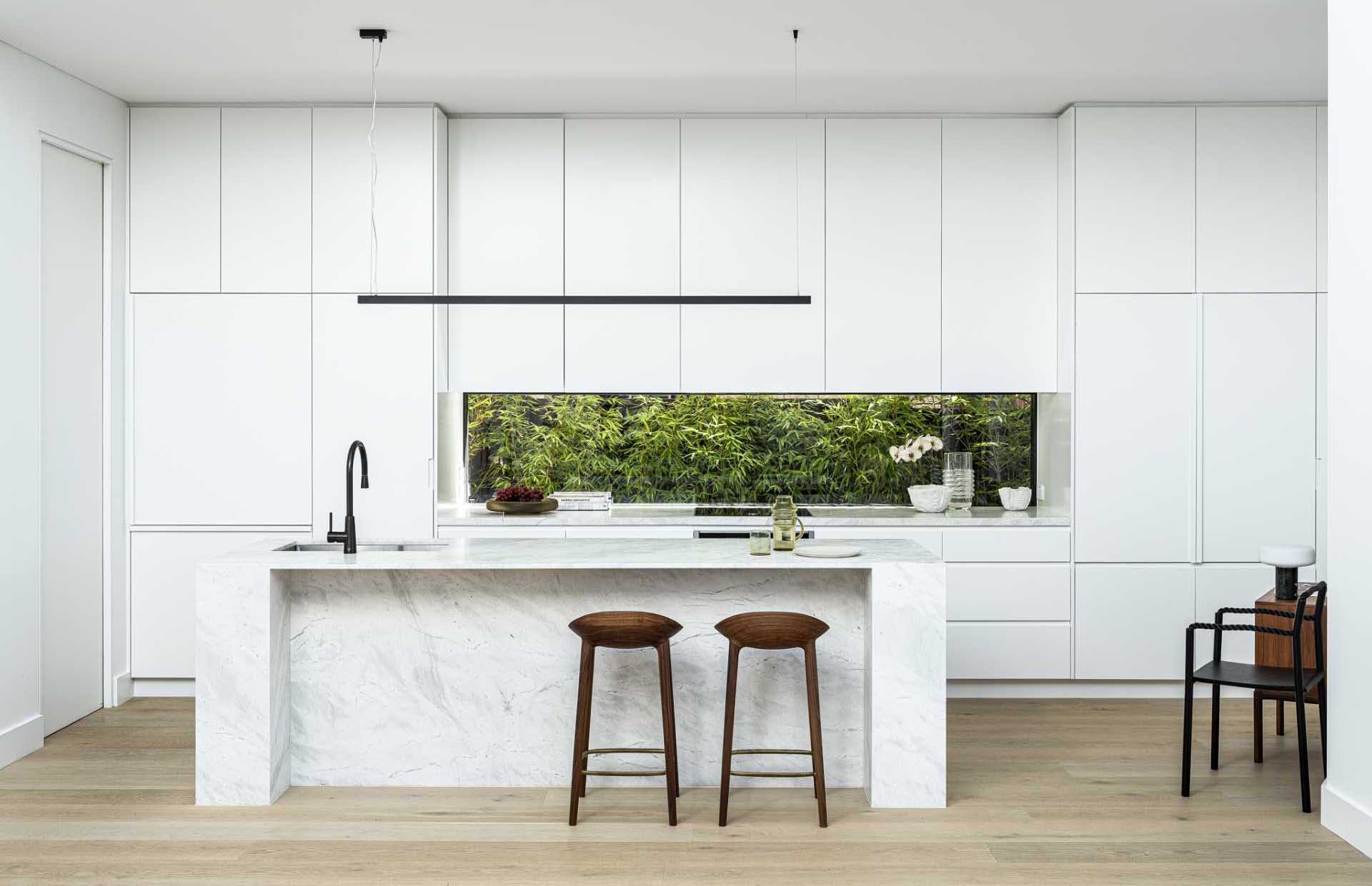 A modern white kitchen with minimalist white cabinets, a window backsplash, and an island.