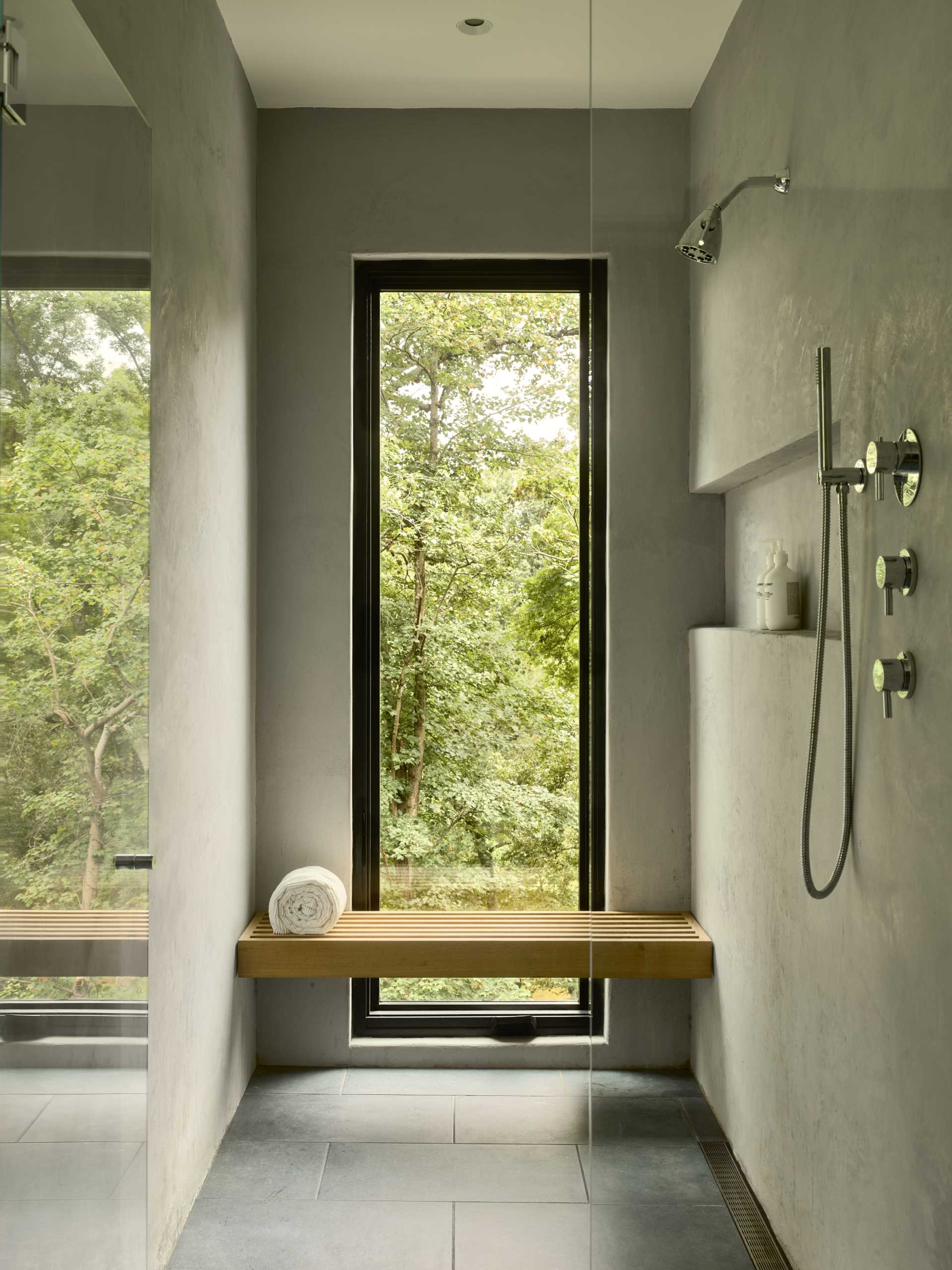 A modern bathroom with a window in the shower that frames the forest view.