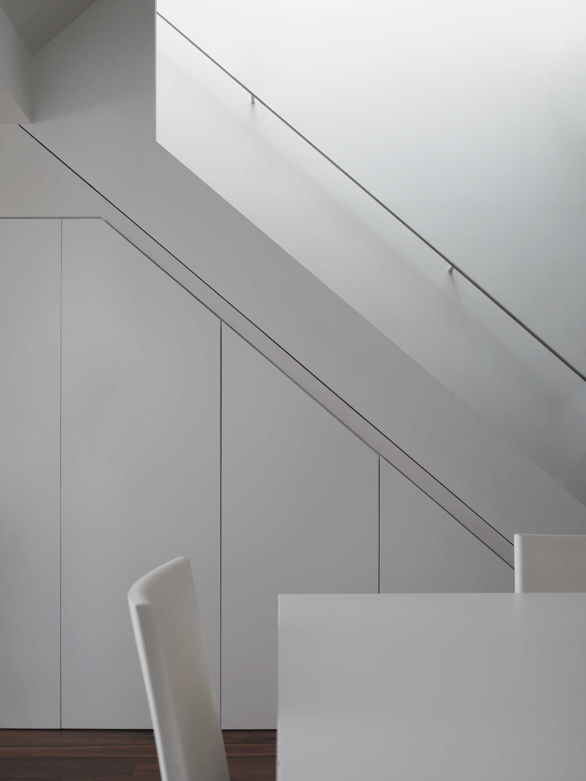 A white dining table and chairs perfectly match the stairs and walls.