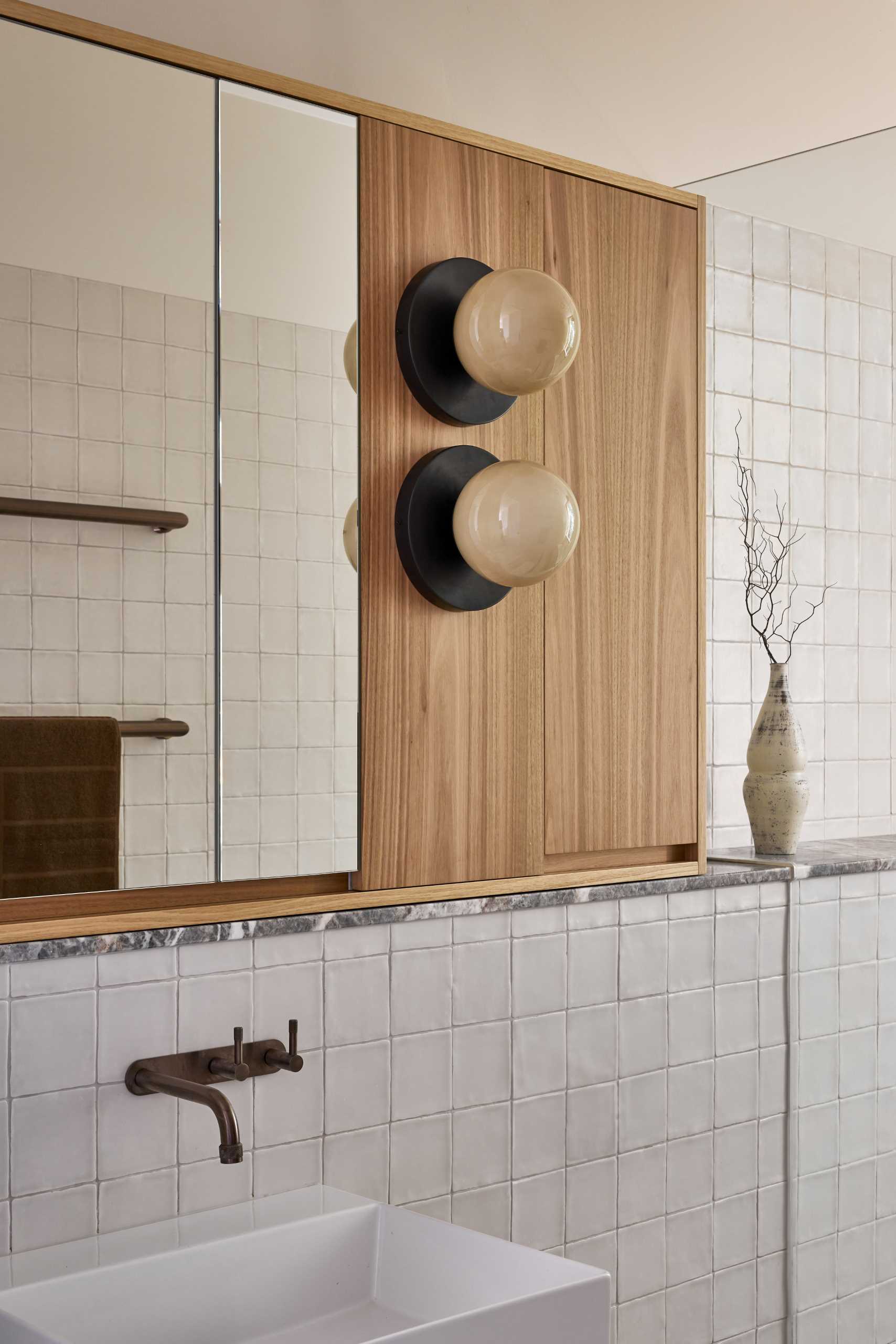 In this bathroom, there's a built-in bathtub next to the shower, while tiles partially cover the walls, and globe lights are positioned next to the mirror.