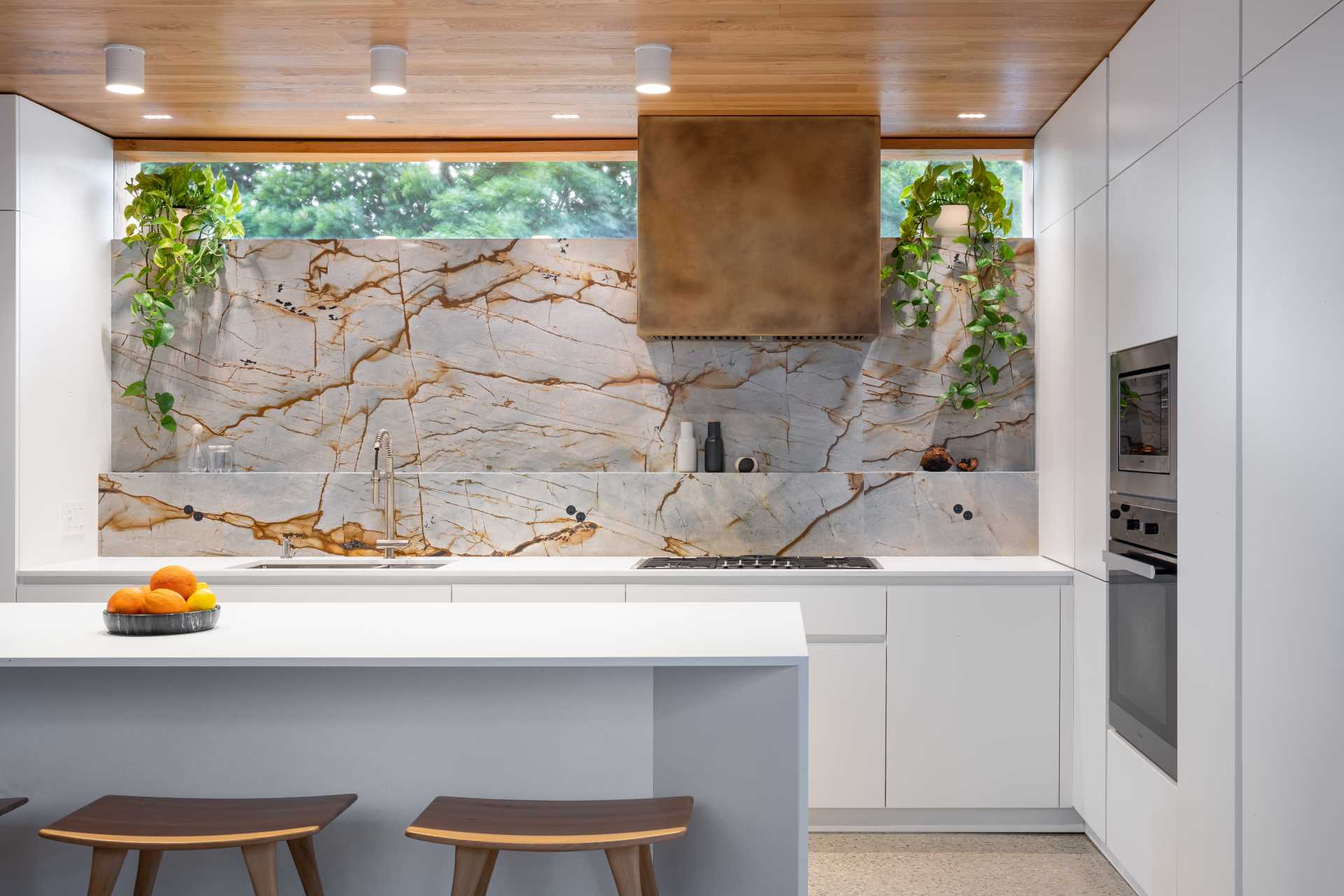 In the kitchen, a stone backsplash continues up the wall, while a window at the top adds natural light, and minimalist white cabinetry features throughout.