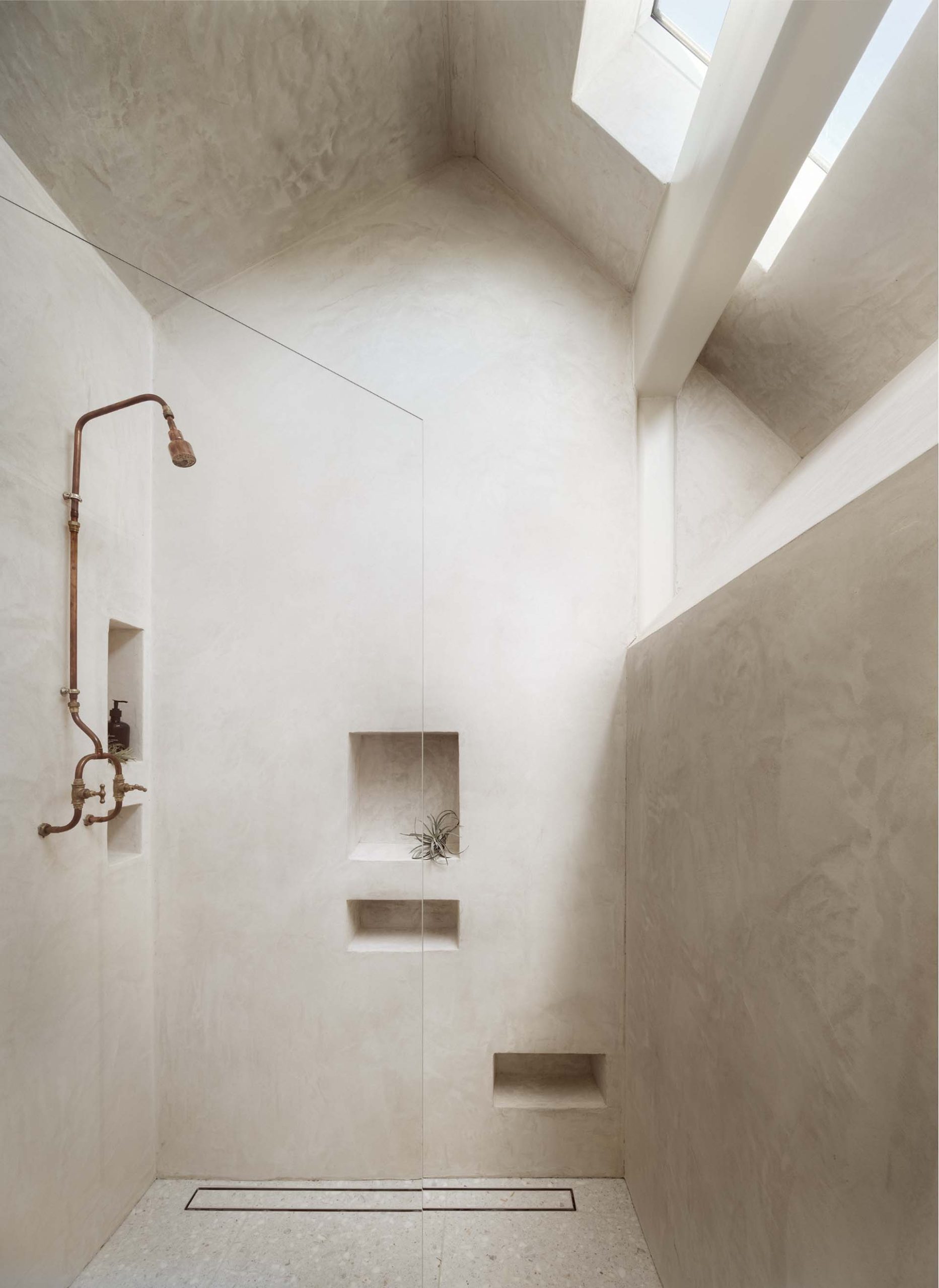 A bathroom includes an angular mirror, a s،wer with shelving niches, and a skylight.