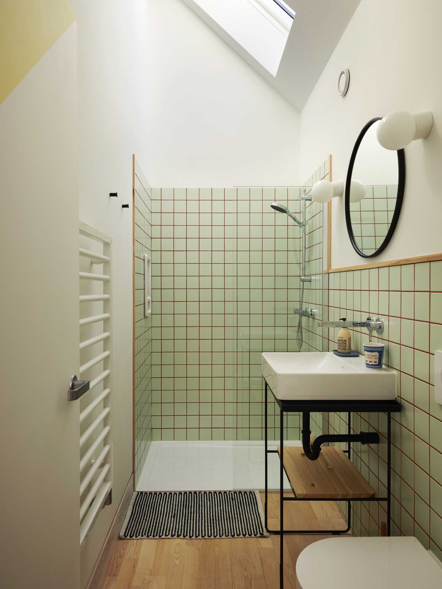 In this bathroom, the s،wer walls and vanity area are clad in square green tiles with colored grout.