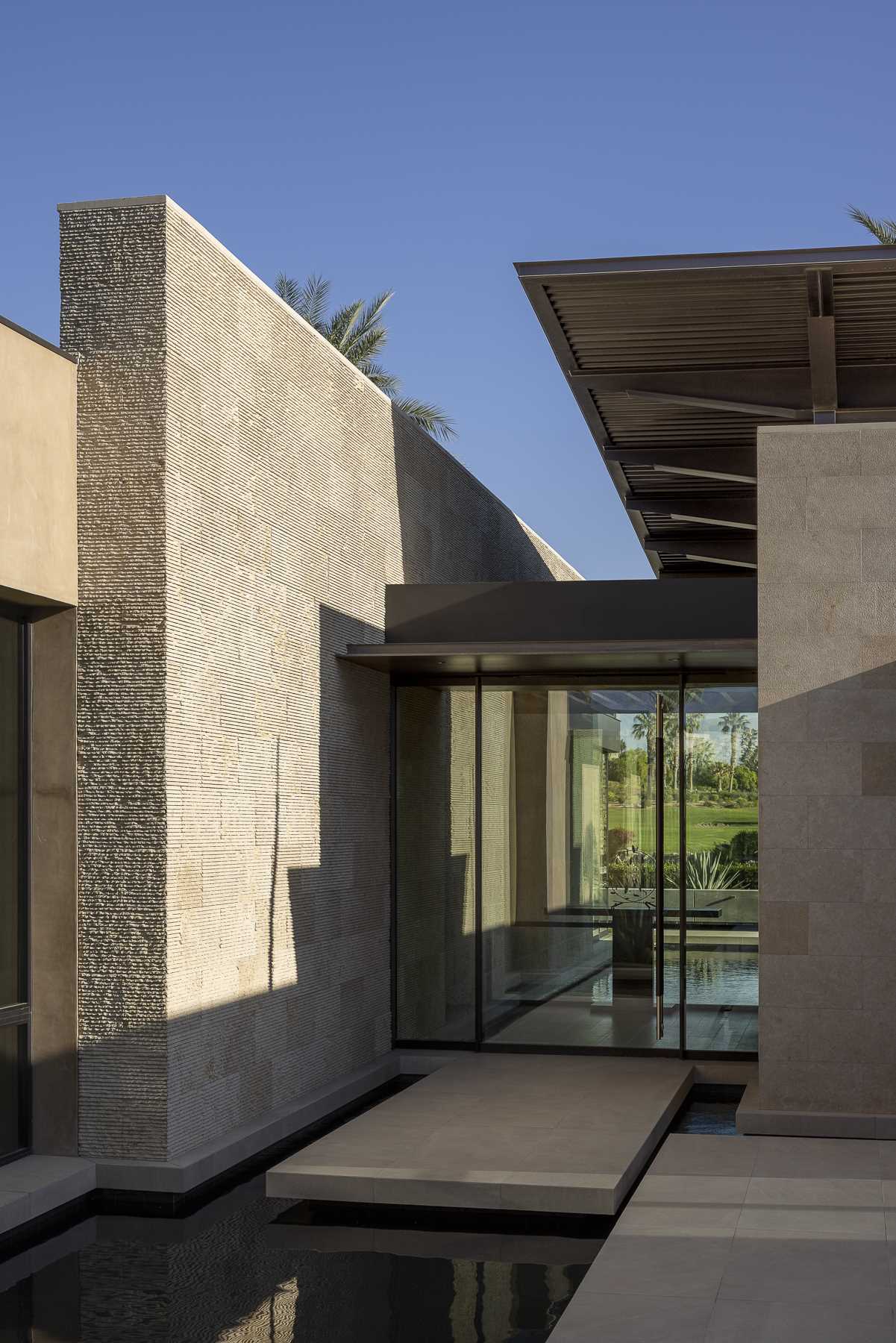A glass front door provides views of the golf course on the other side of the home, while exterior stone seamlessly extends into the interior, blurring the distinction between indoor and outdoor spaces.