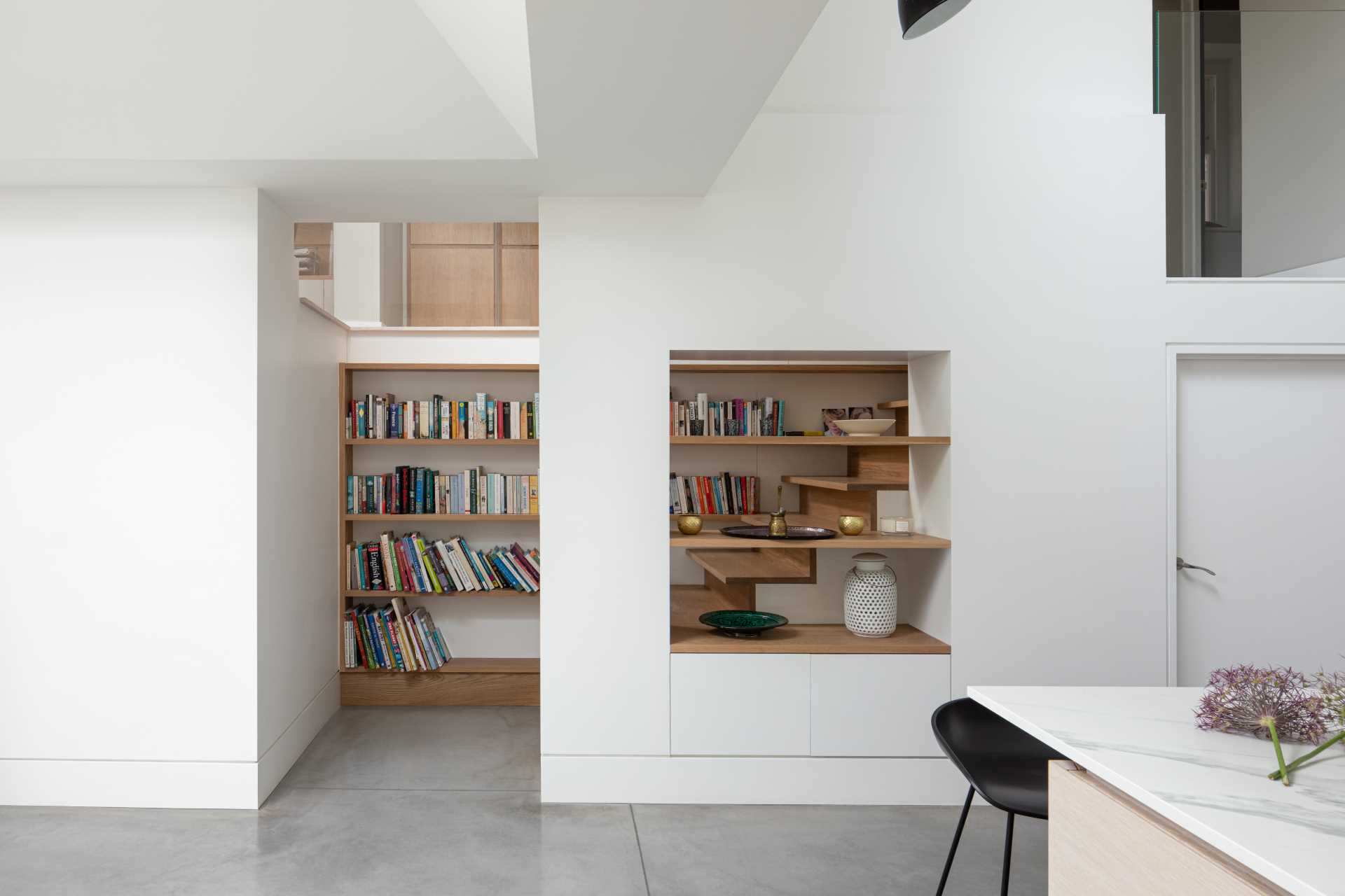 A wood bookshelf is positioned along the stairs, while a small cut-out has mat،g wood shelves.