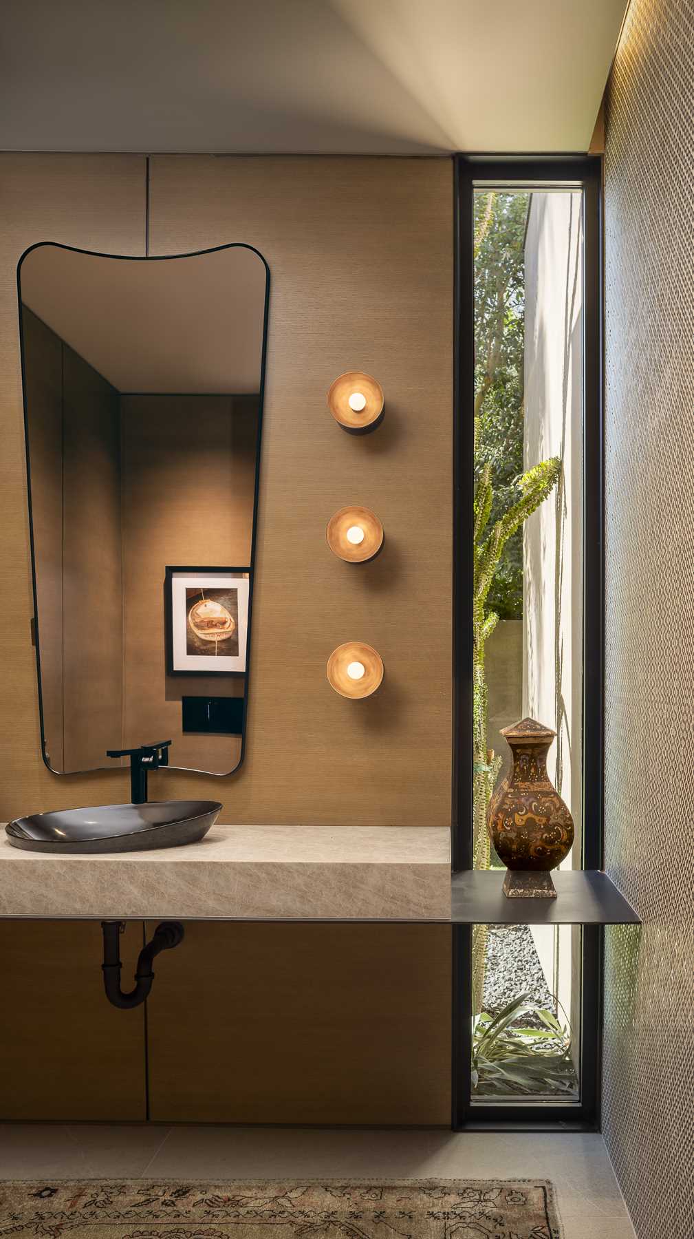 In a powder room, a vertical window gives a glimpse of the outdoors, while a uniquely shaped mirror and wall lights add interest.