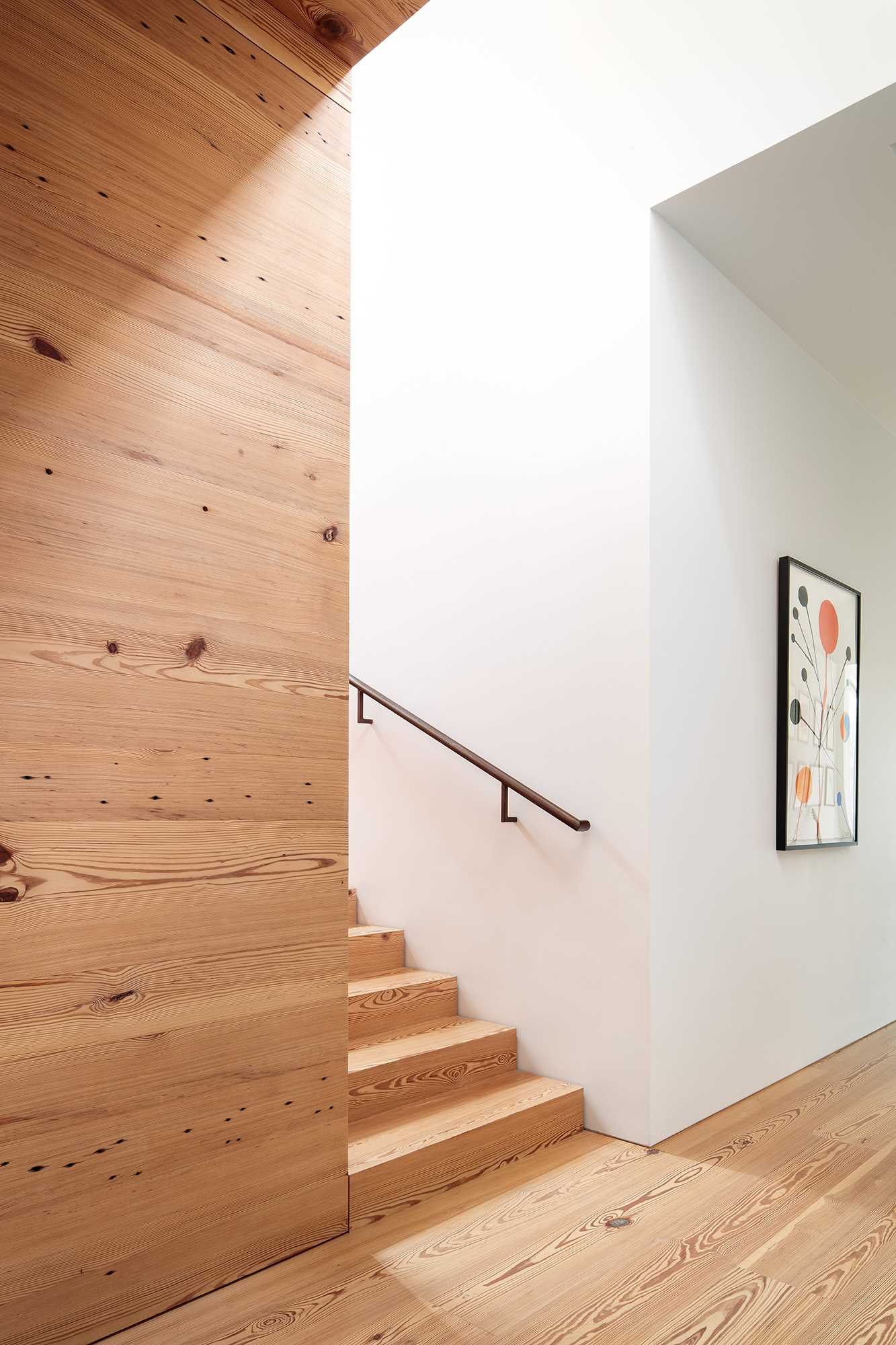 Finished with the same reclaimed long-leaf pine as the floors, the stairs are bathed in light from a clerestory window above a fluorescent artwork, and the weathering steel handrails conceal LED strip lights.
