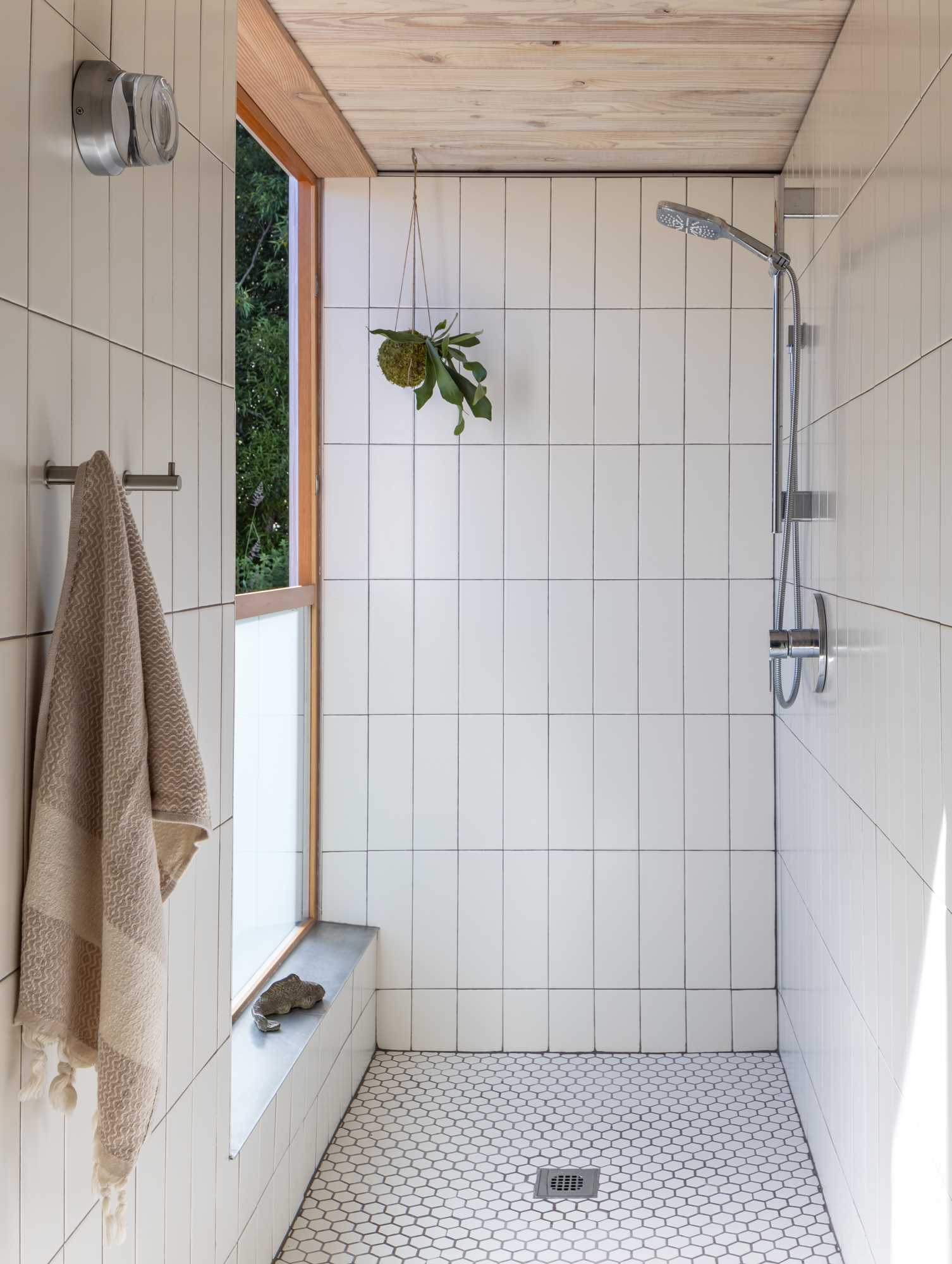 In this bathroom, the walls and floors of the shower are covered by tile, and a window opens for tree views.