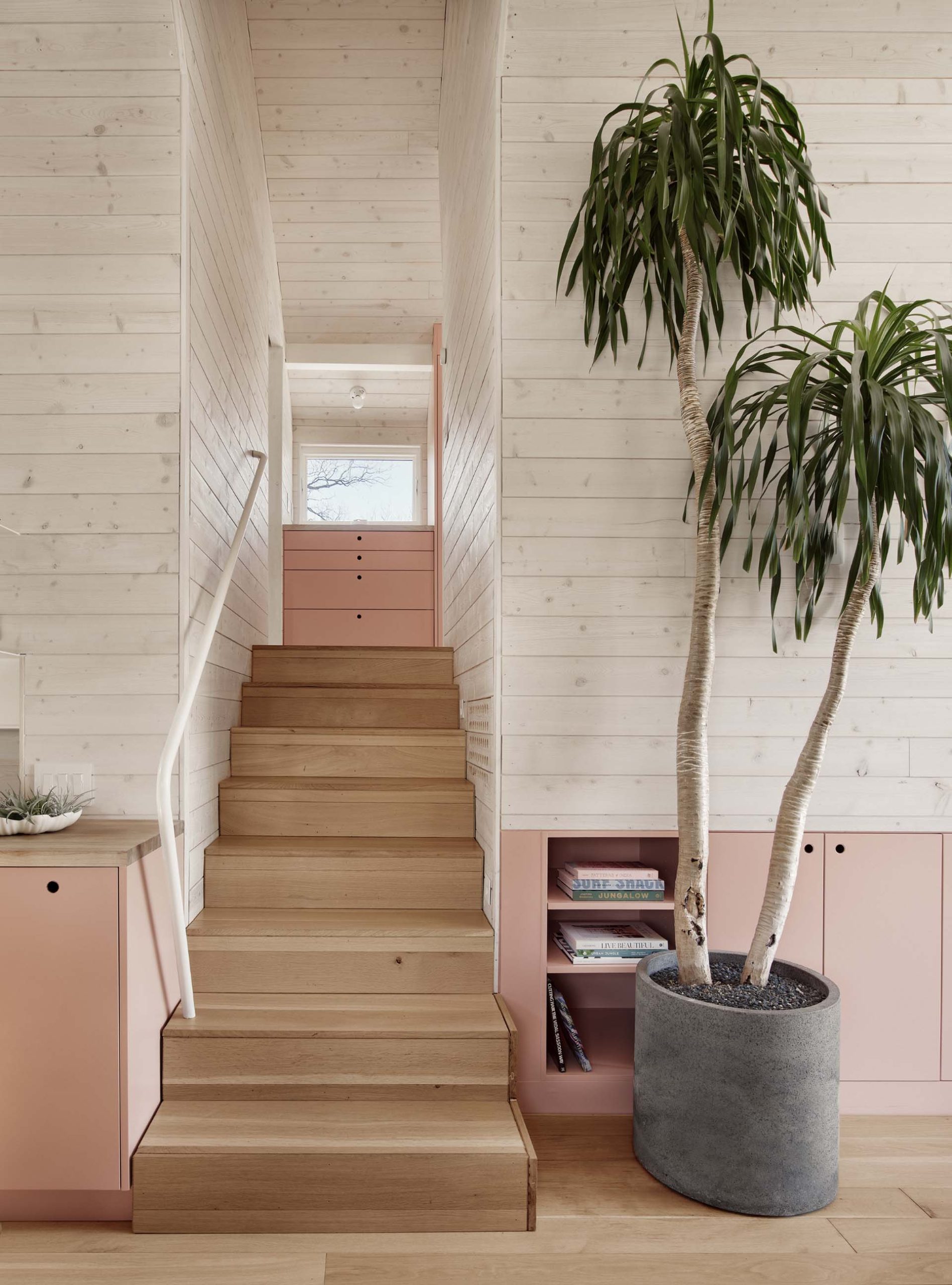 A modern interior with wood floors includes pastel pink cabinetry.