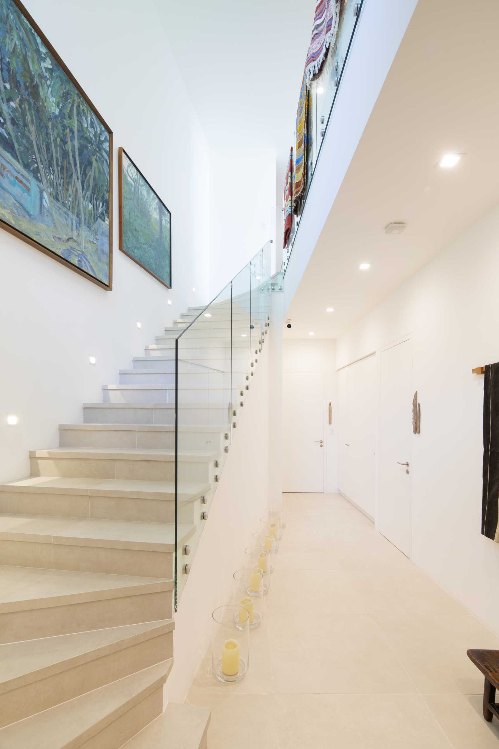 Stairs with a glass railing are decorated with artwork and rugs.