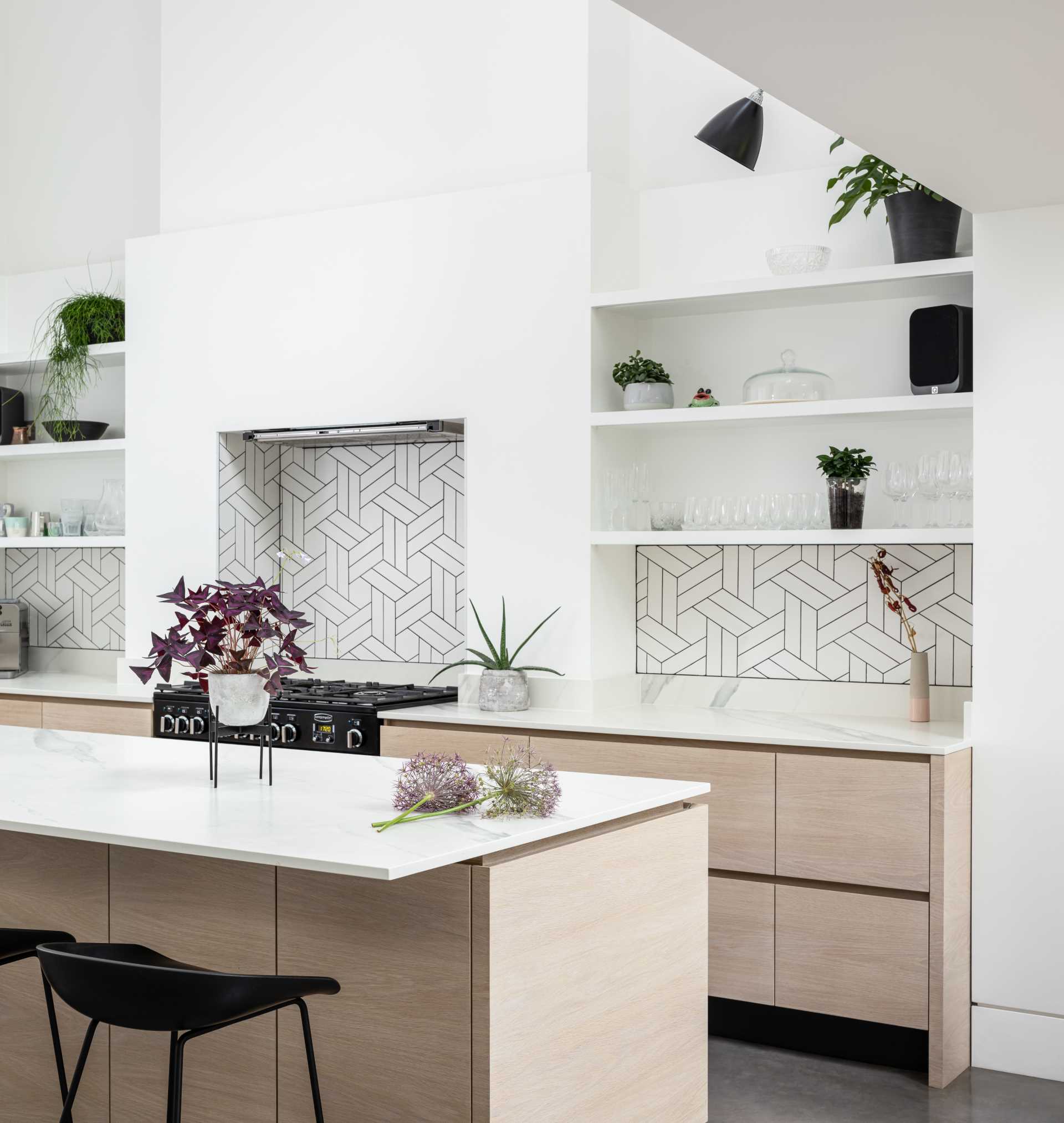 In the kitchen white walls and shelving are complemented by geometric tiles with dark grout and hardware-free wood cabinetry.