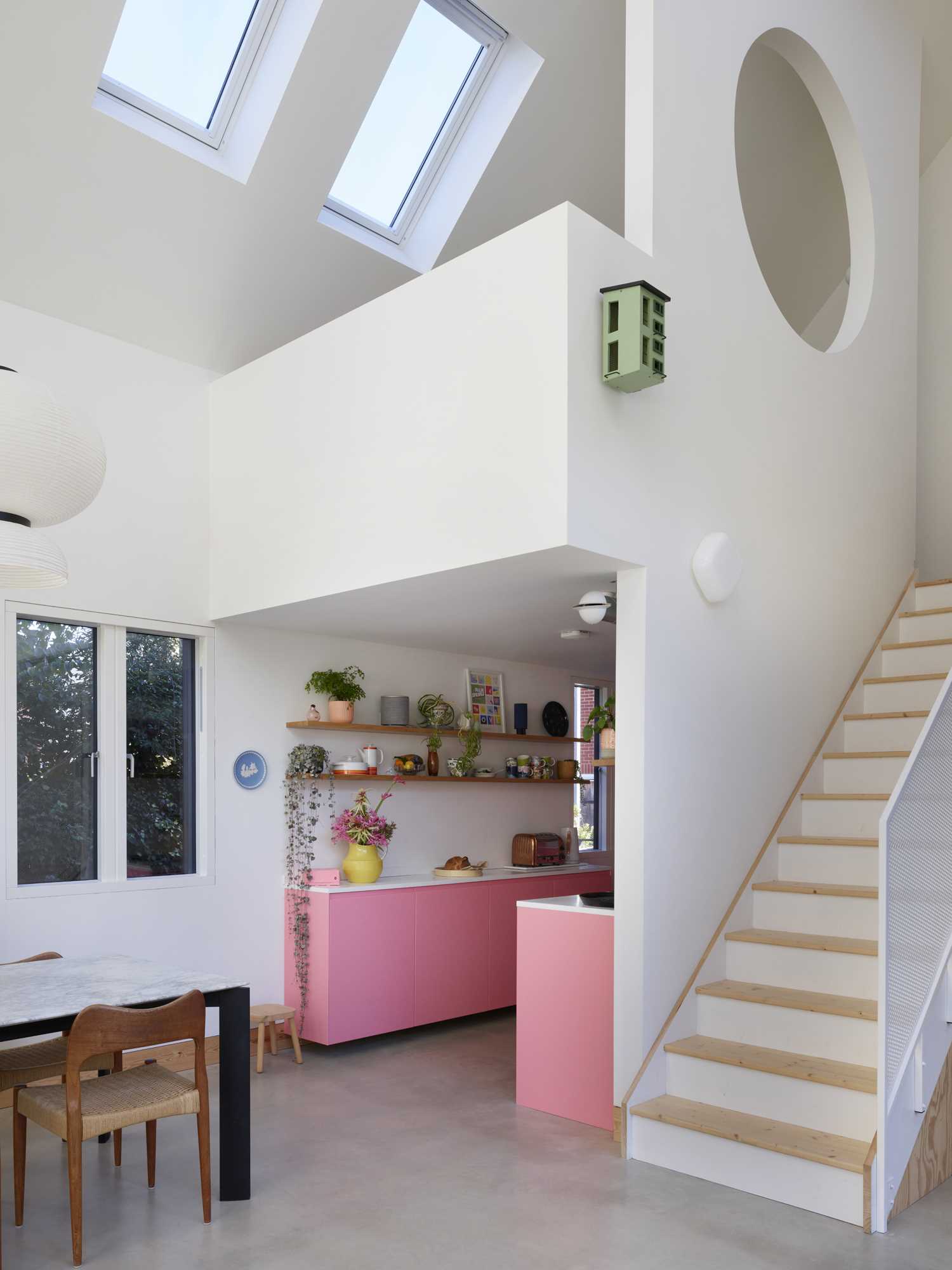 An unexpected design detail in this contemporary home is the kitchen with its pink cabinets, which are complemented by white countertops and floating wood shelves.