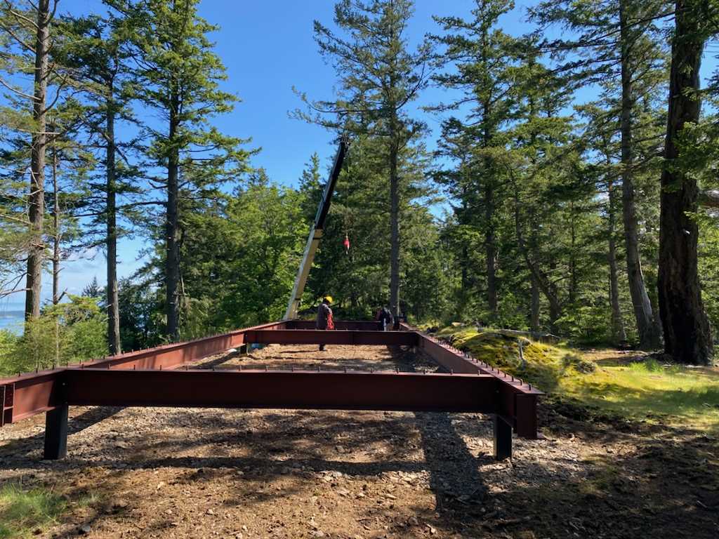 Construction photos of a modern island home with a cantilevered design, wood siding, and a standing seam metal roof.