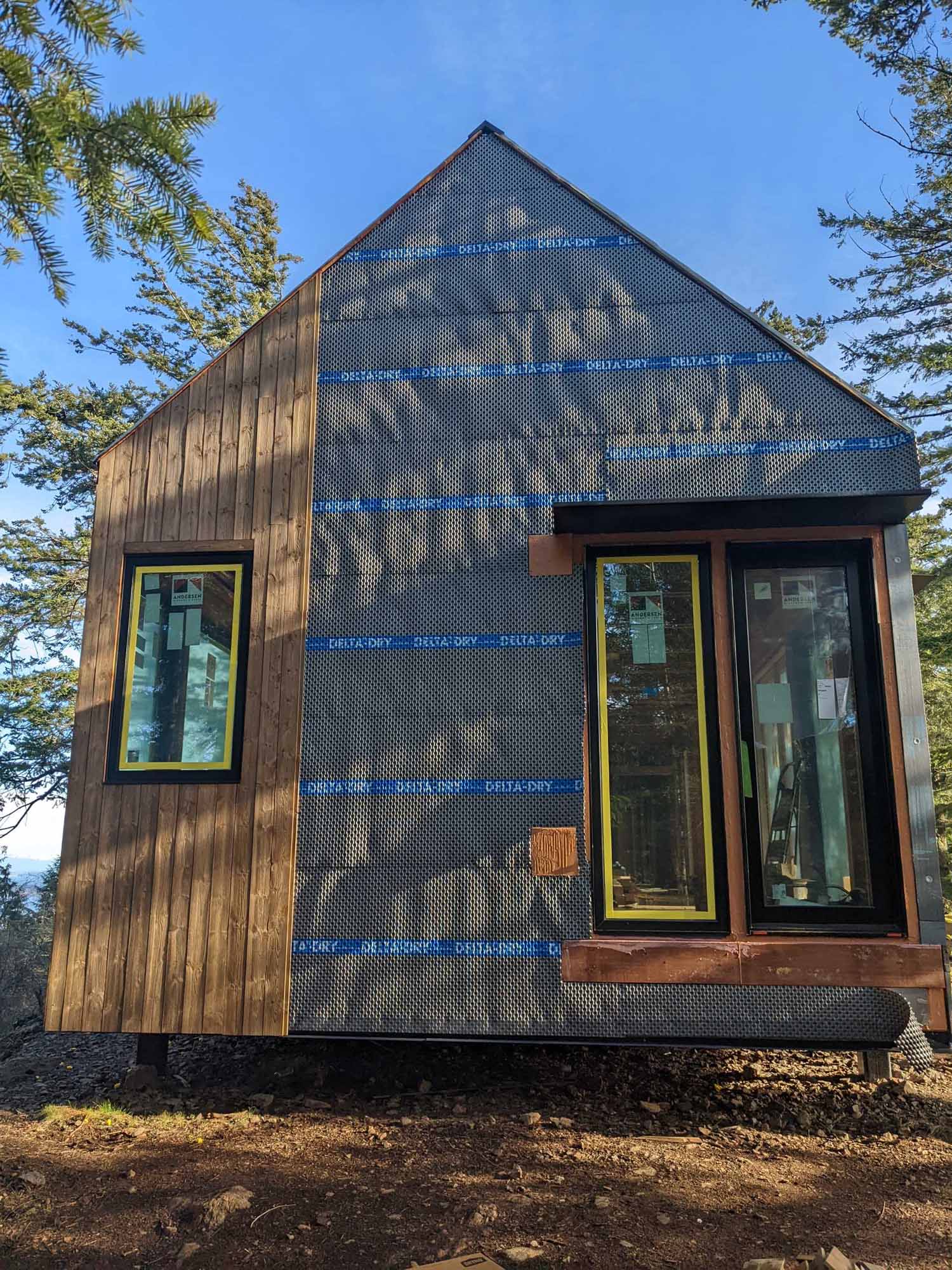 Construction photos of a modern island home with a cantilevered design, wood siding, and a standing seam metal roof.