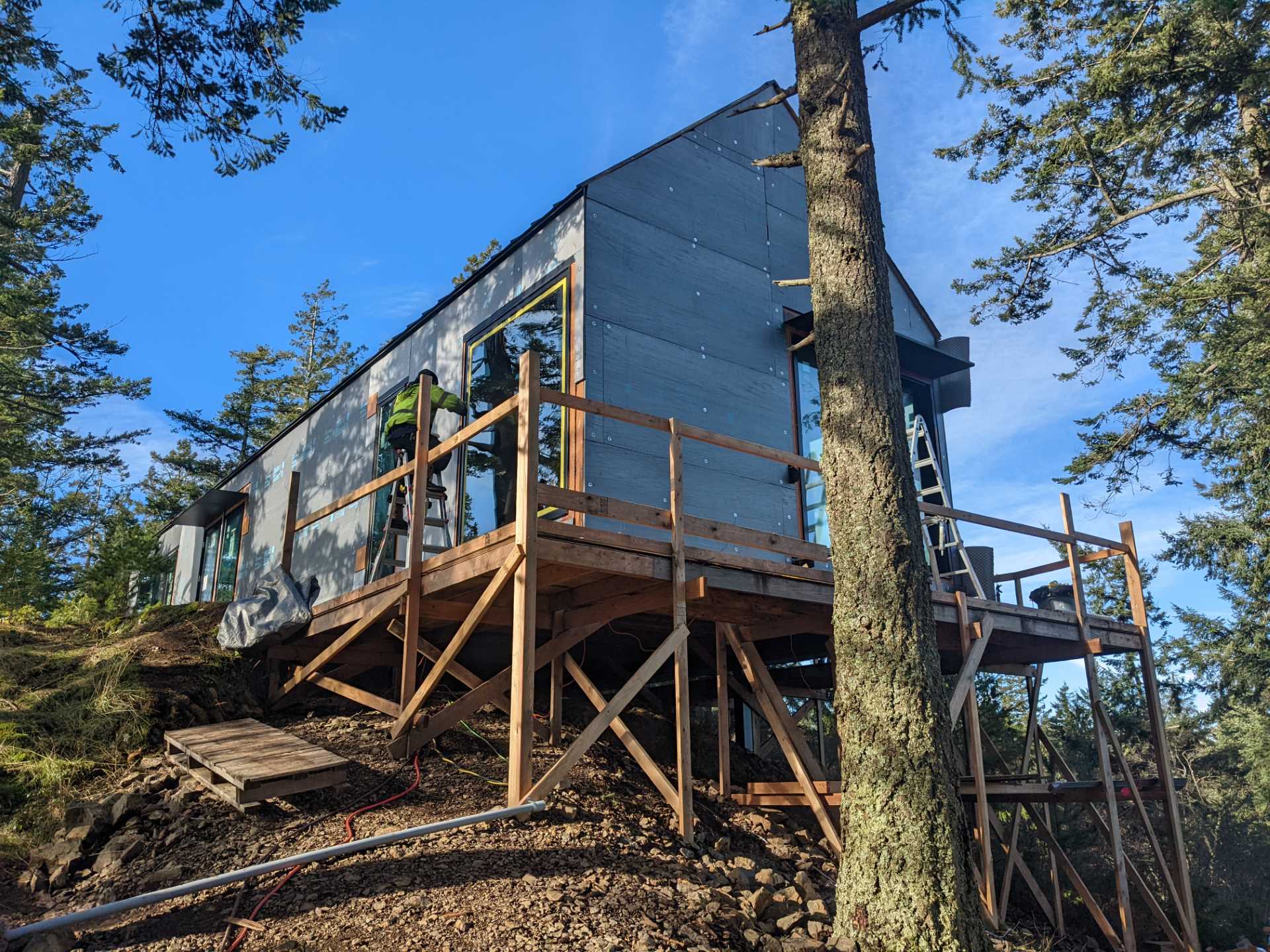 Construction photos of a modern island home with a cantilevered design, wood siding, and a standing seam metal roof.