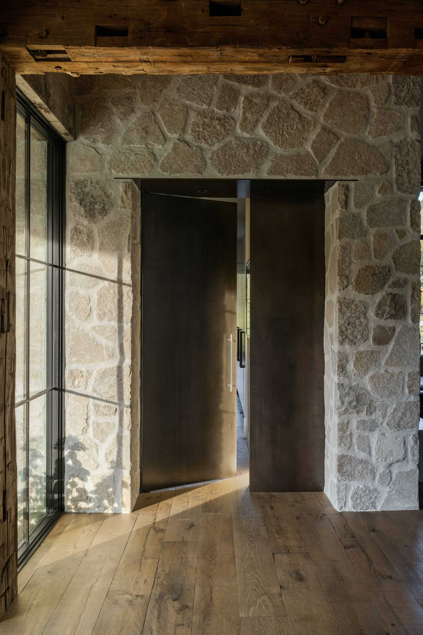 Steel doors, stone, antique flooring, floor-to-ceiling windows, and rustic hand-hewn timbers create a unique and warm interior for this contemporary ranch home.