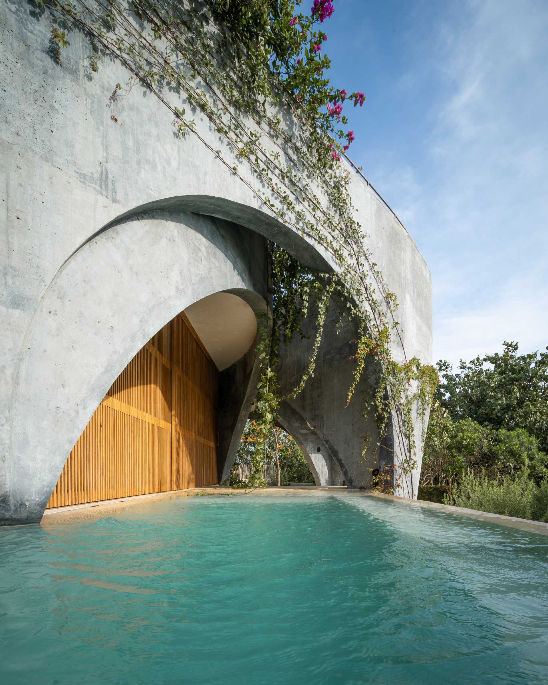 A modern concrete home with a round design, open arches, and a swimming pool.