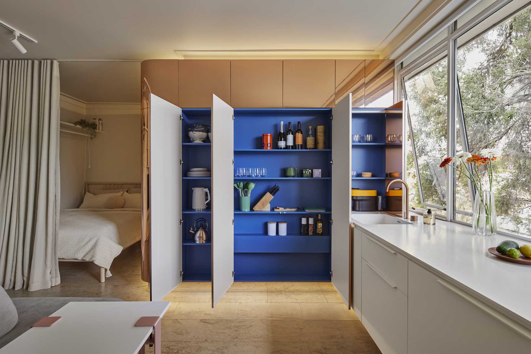 In the kitchen of this micro apartment, the brass pod opens to reveal blue kitchen shelves, adding a hidden pop of color to the interior.