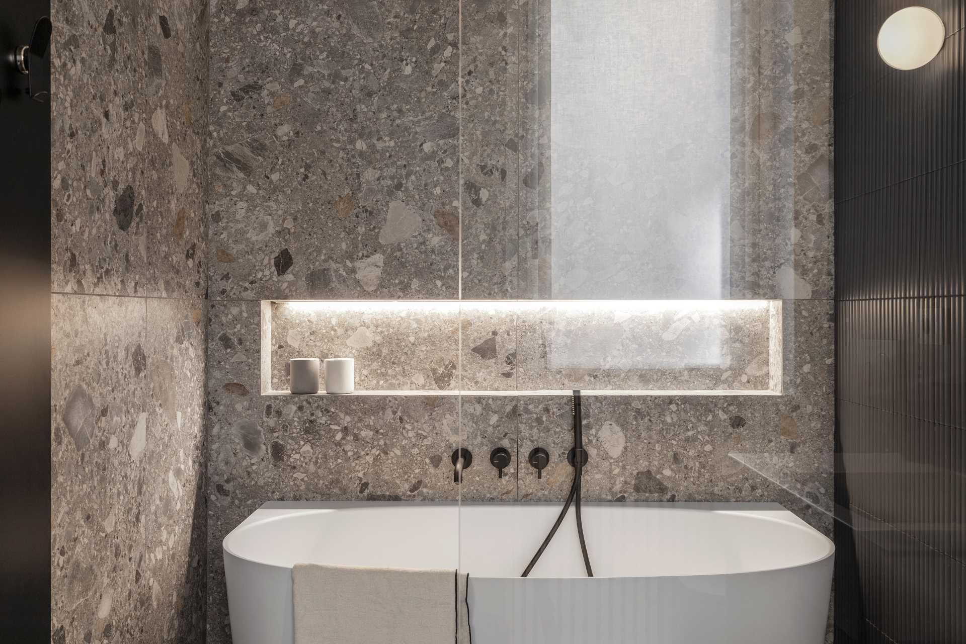 This primary en-suite bathroom has a wall of gunmetal tiles that complements the Ceppo di Grè stone, both on the floor and vertically around the freestanding tub.