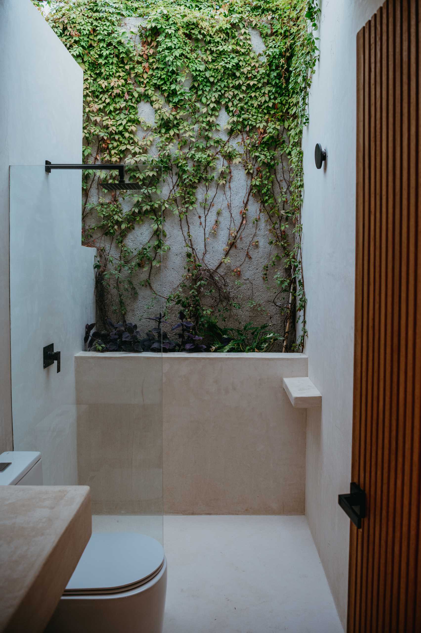 A modern bathroom includes a wall with ivy, creating a feeling of being outdoors.