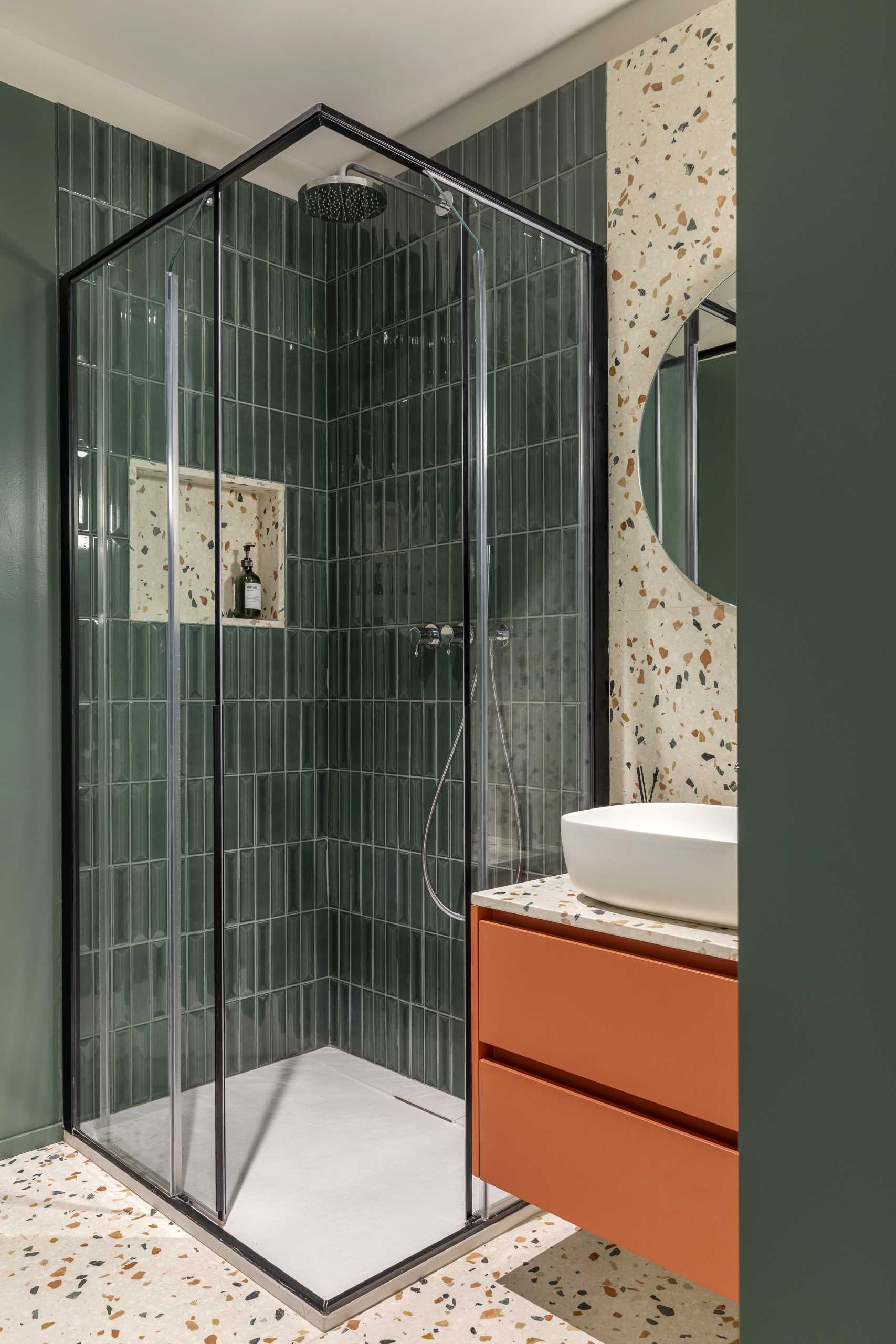 In this guest bathroom, deep green is the chosen color for the tiles and walls, complimenting the various colors found in the Terrazzo resin marble used for the vanity and wall behind the mirror.
