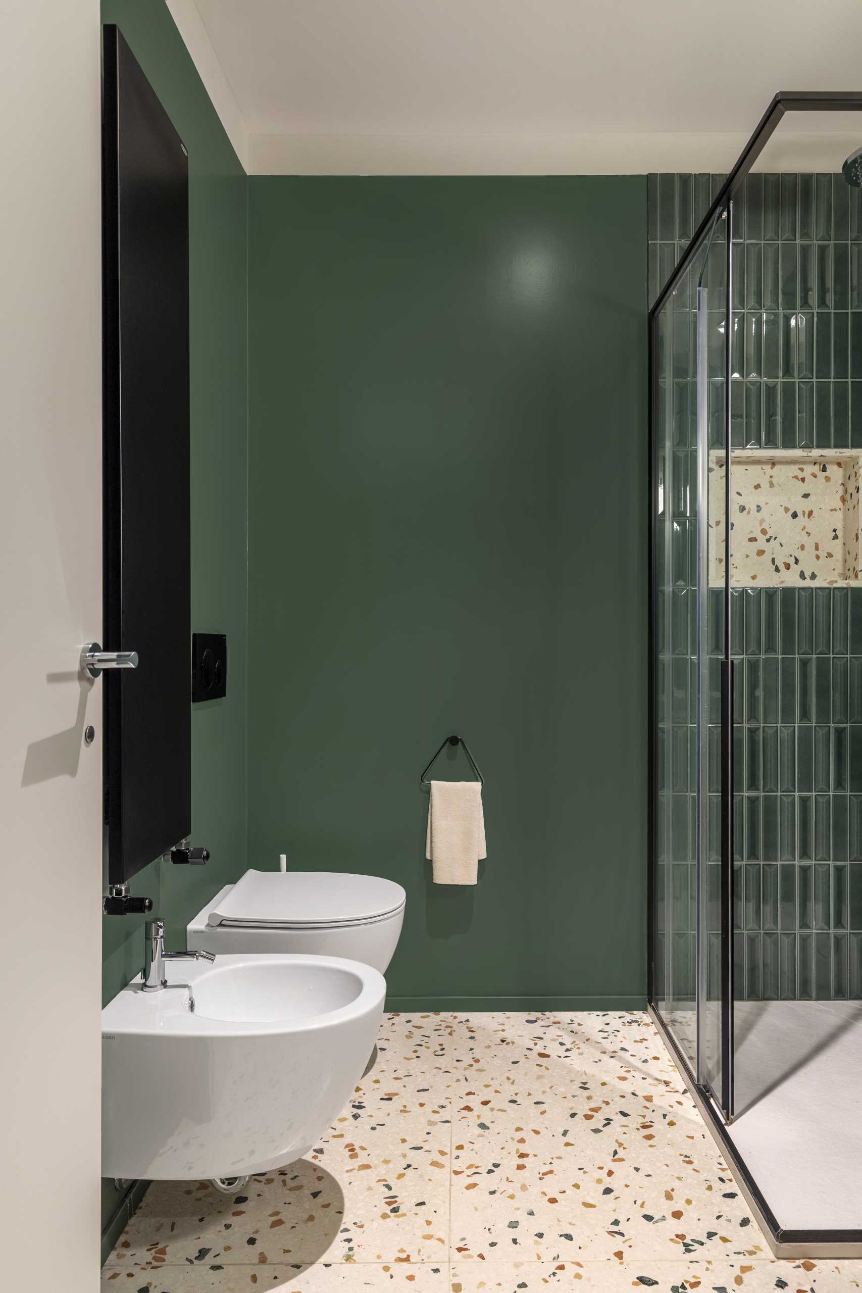 In this guest bathroom, deep green is the chosen color for the tiles and walls, complimenting the various colors found in the Terrazzo resin marble used for the vanity and wall behind the mirror.