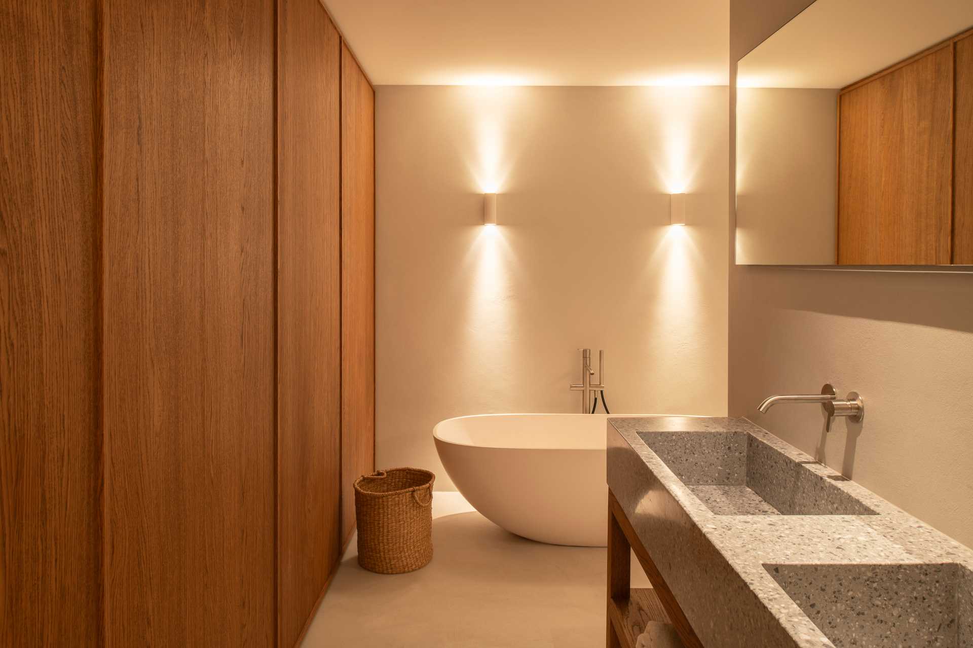 In this modern bathroom, a double vanity is made from Terrazzo, while the wood walls complement the other wood features in the home, and a freestanding bathtub allows for relaxation.