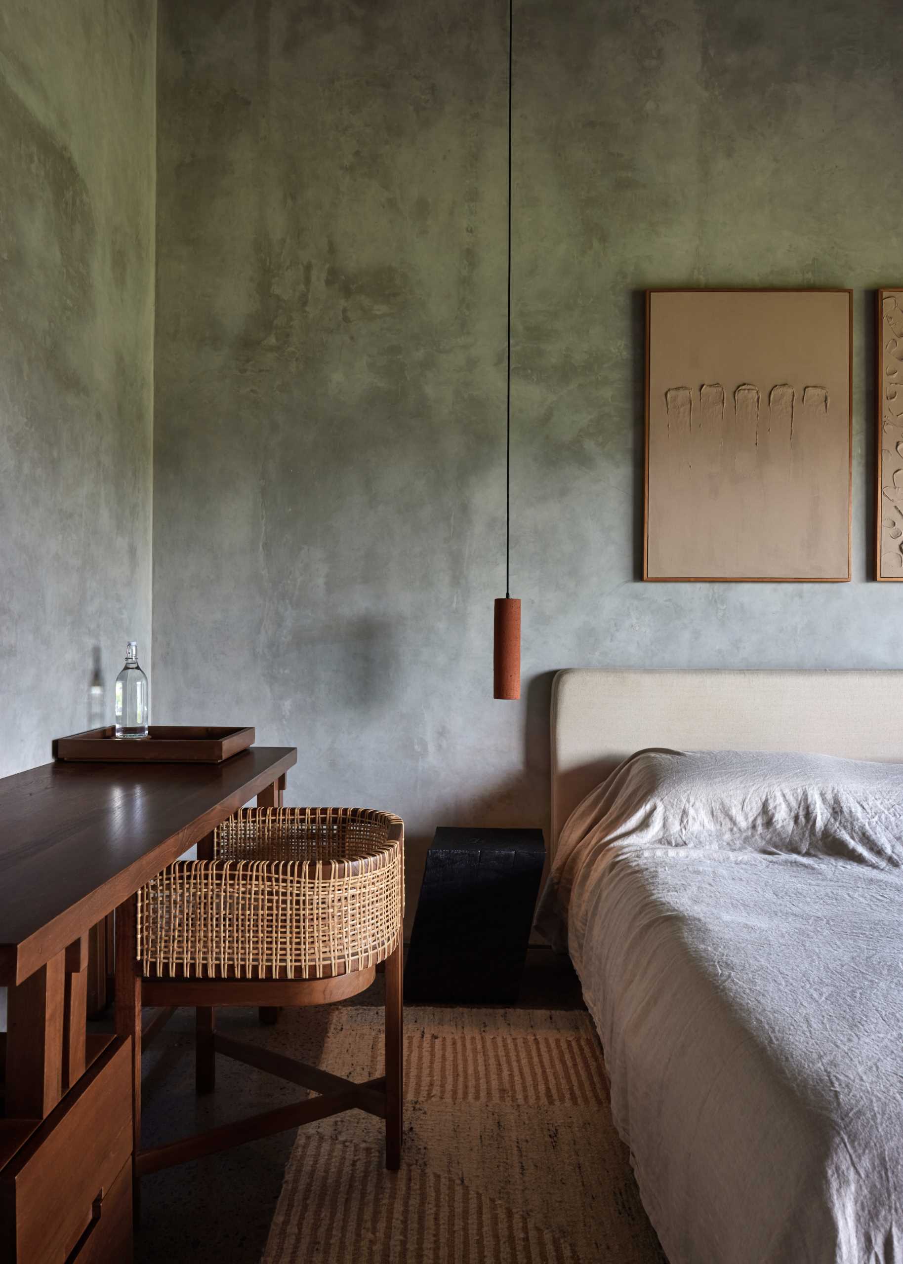 A bedroom with a minimalist look includes simple wood furniture and a pendant light that acts as a bedside lamp.