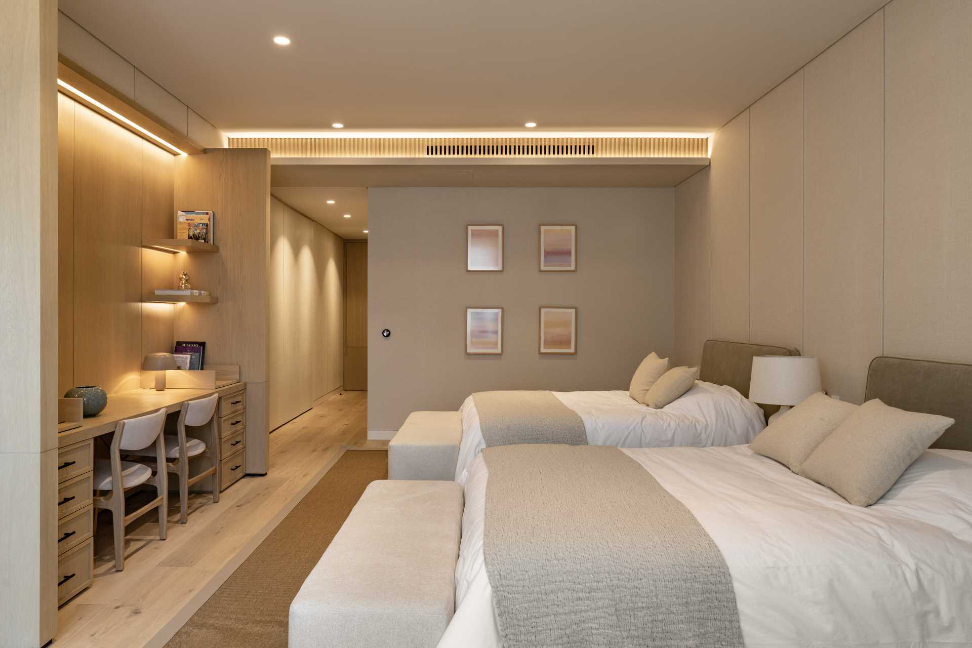 A modern bedroom with two beds includes a long desk and hidden lighting.