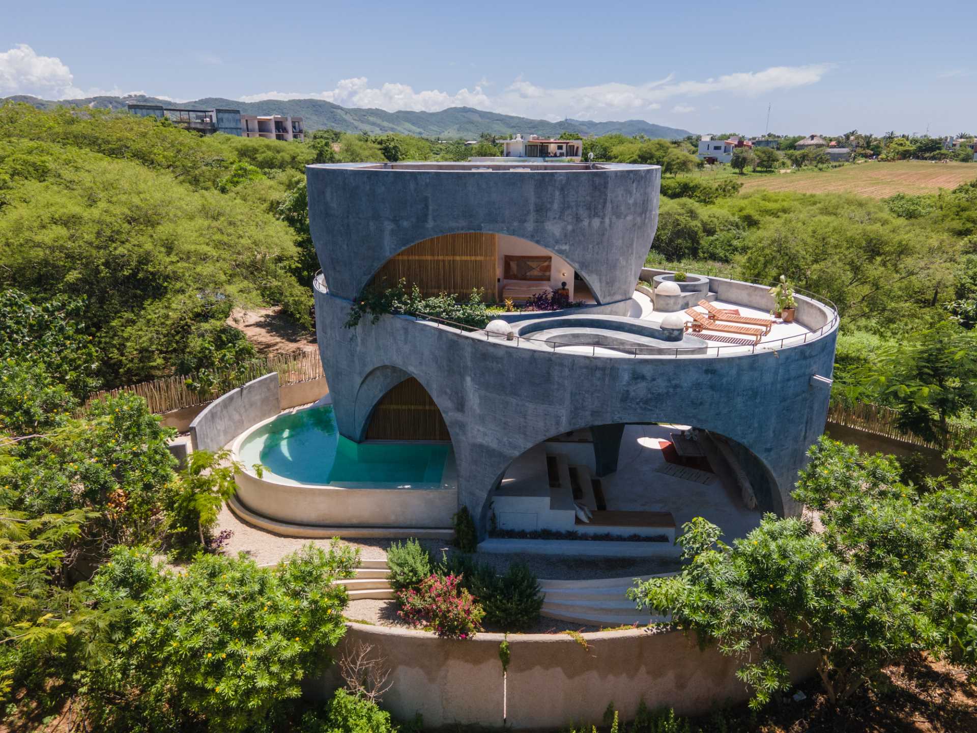 A modern concrete home with a round design, open arches, and a swimming pool.