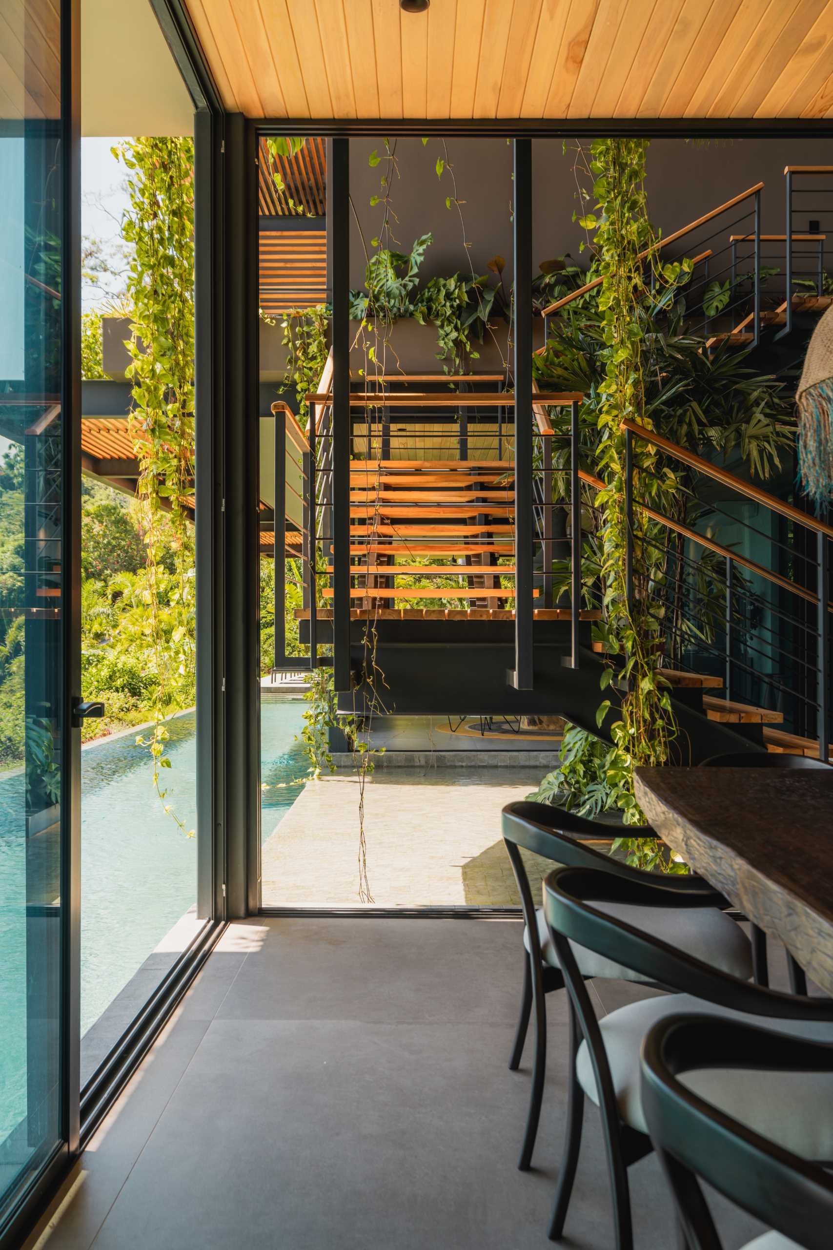 A modern open-plan dining area opens to the swimming pool and atrium with stairs.