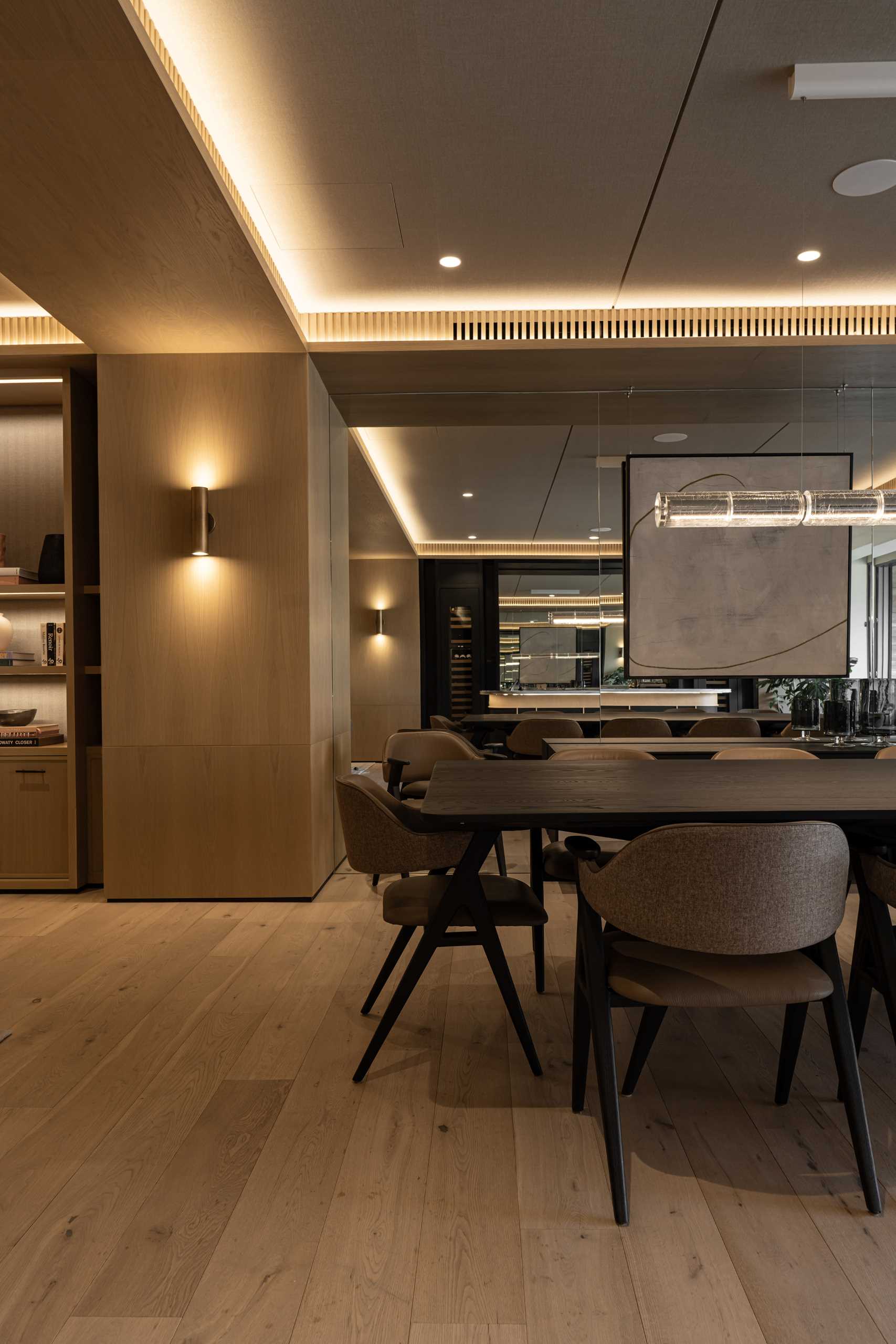 This open-plan dining room has a mirrored wall and features the Luana chair from Piztola, with its dark wood and leather tones, adding a touch of sophistication.