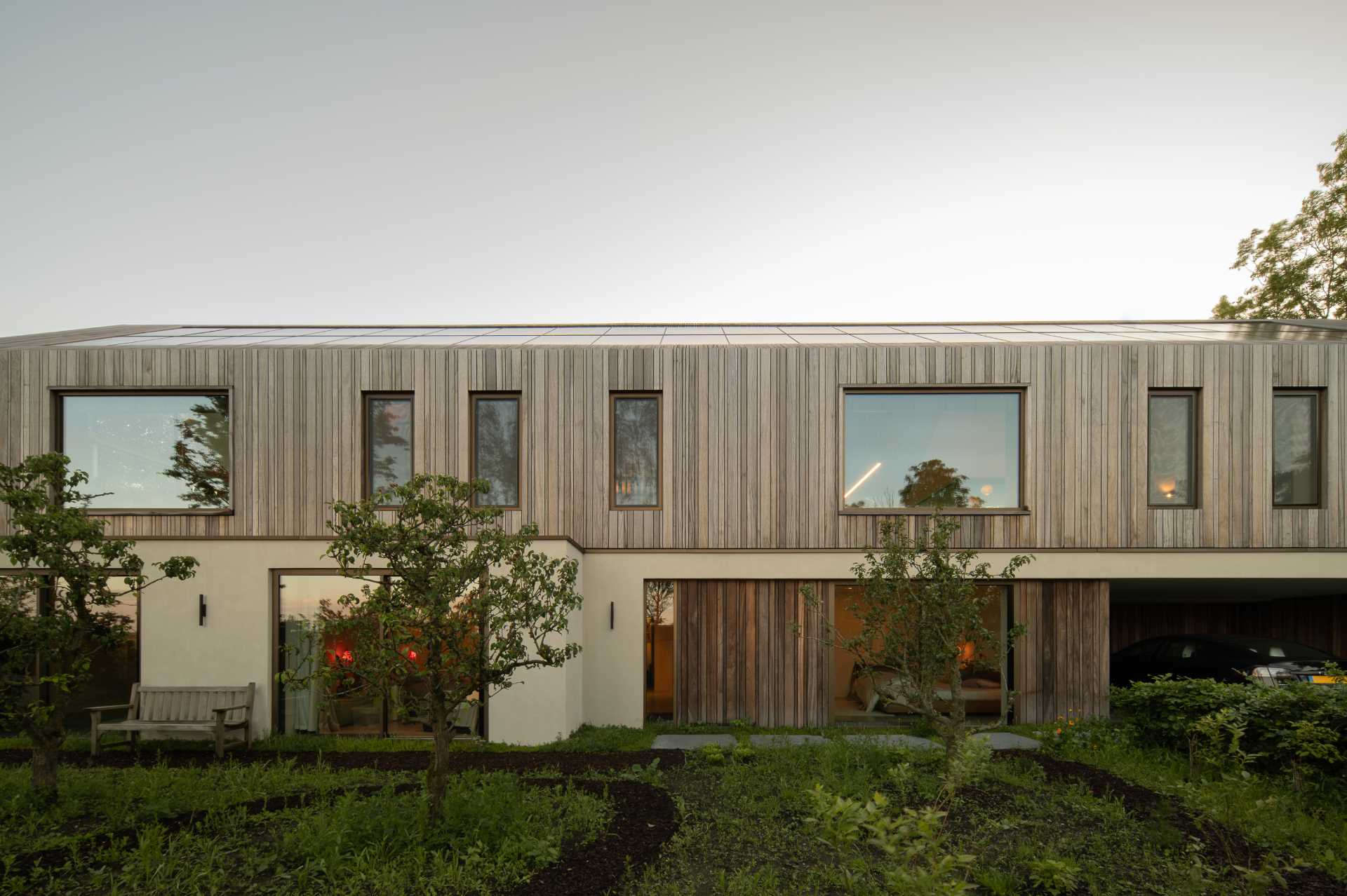 The entrance facade of this modern home combines the Padoek wood siding with stucco for a modern appearance. At night, lighting is used to highlight the design.