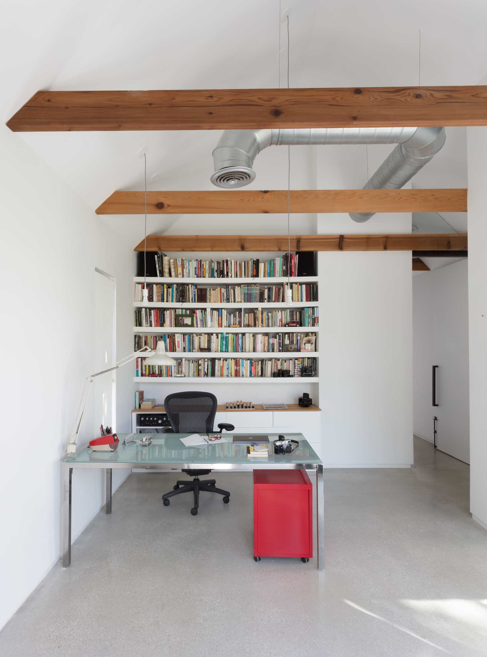 This modern home office/studio features exposed wood beams, concrete floors, and built-in shelves.