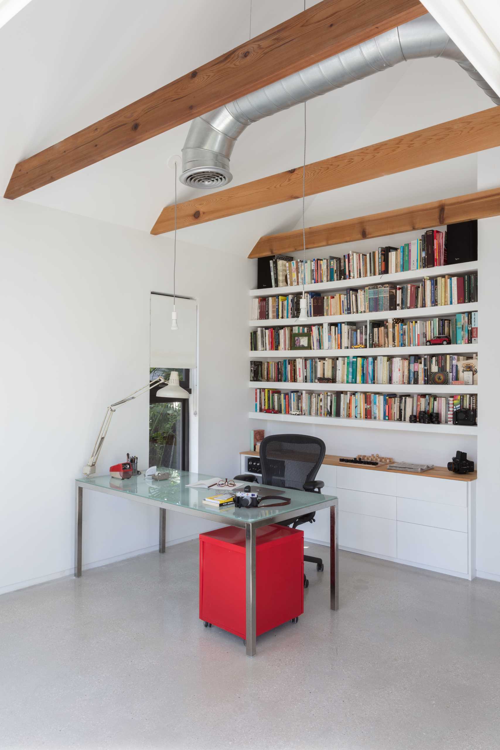 This modern home office/studio features exposed wood beams, concrete floors, and built-in shelves.