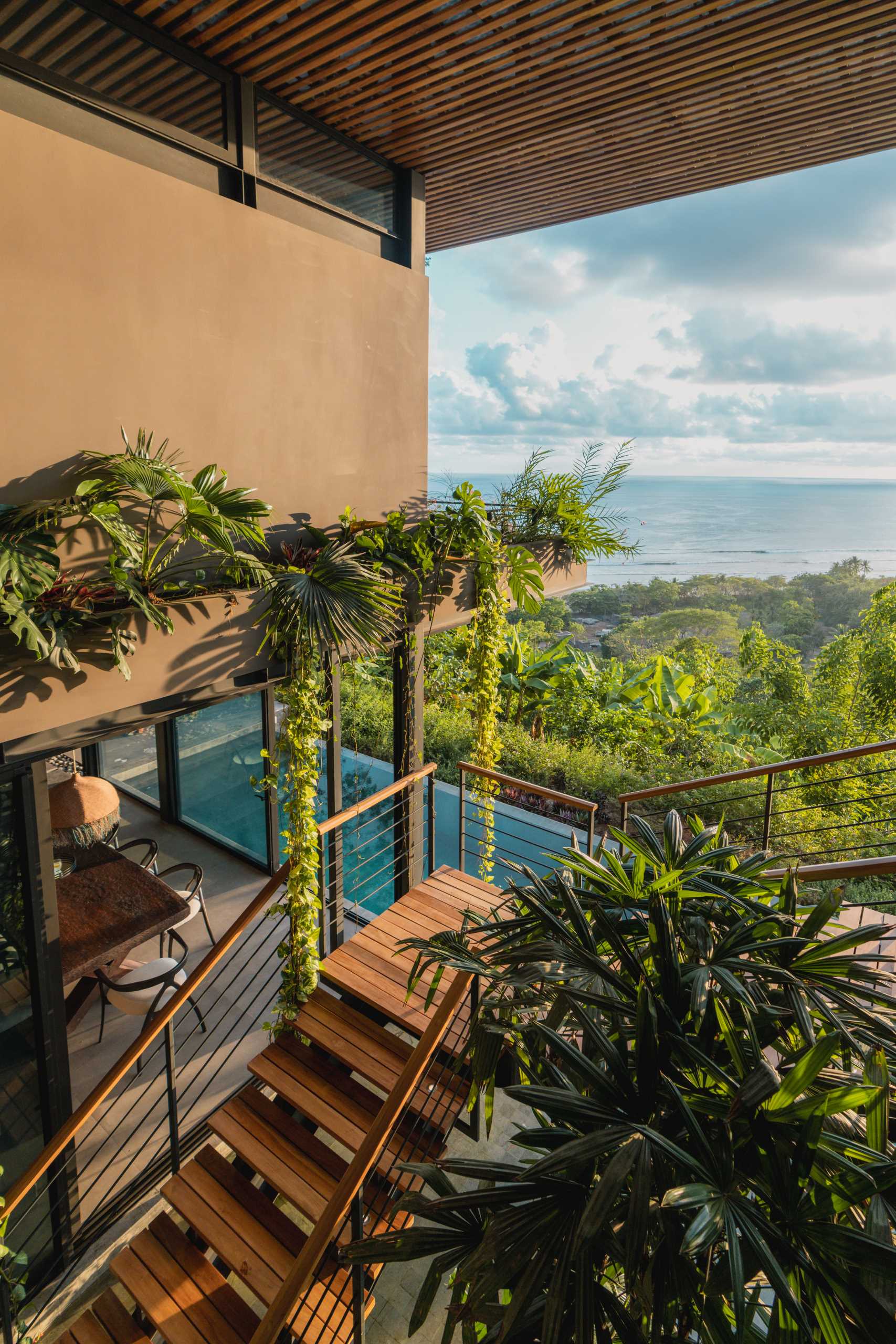 The two levels of this modern tropical home are connected by an open staircase in a central atrium, suspended over a shallow extension of the pool.