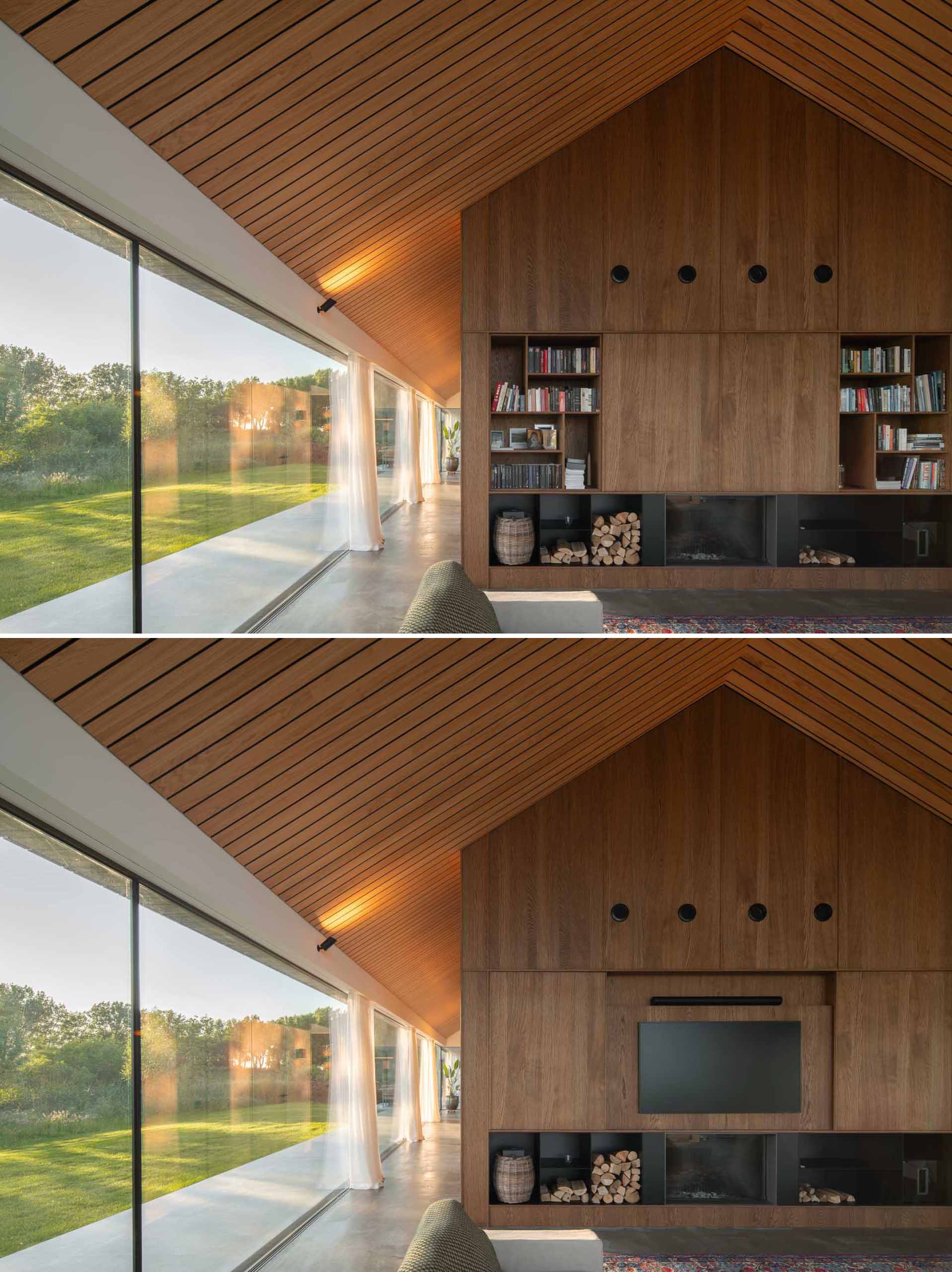 In the living room, it's easy to see the wood-lined gabled ceiling of this modern home. The living room includes sliding doors at one end, a fireplace with wood storage, and a custom shelving unit with a hidden TV.