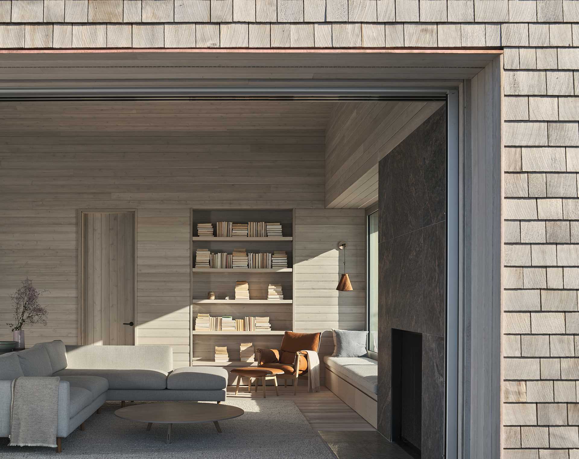 A modern cottage has a living room with a fireplace, a window seat, and a built-in bookshelf.