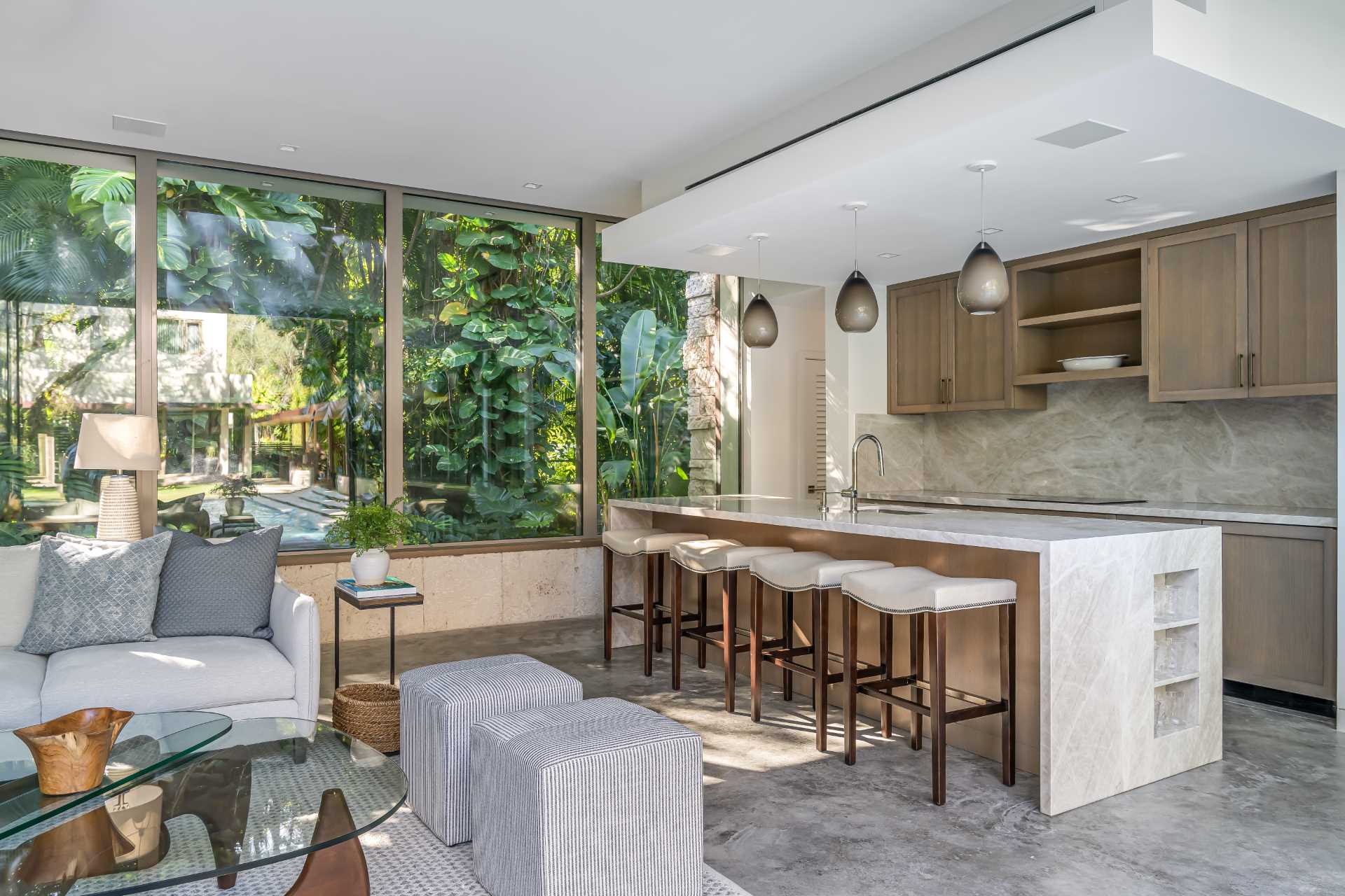 A modern backyard pavilion includes a kitchen with wood cabinetry, an island, and stool seating.