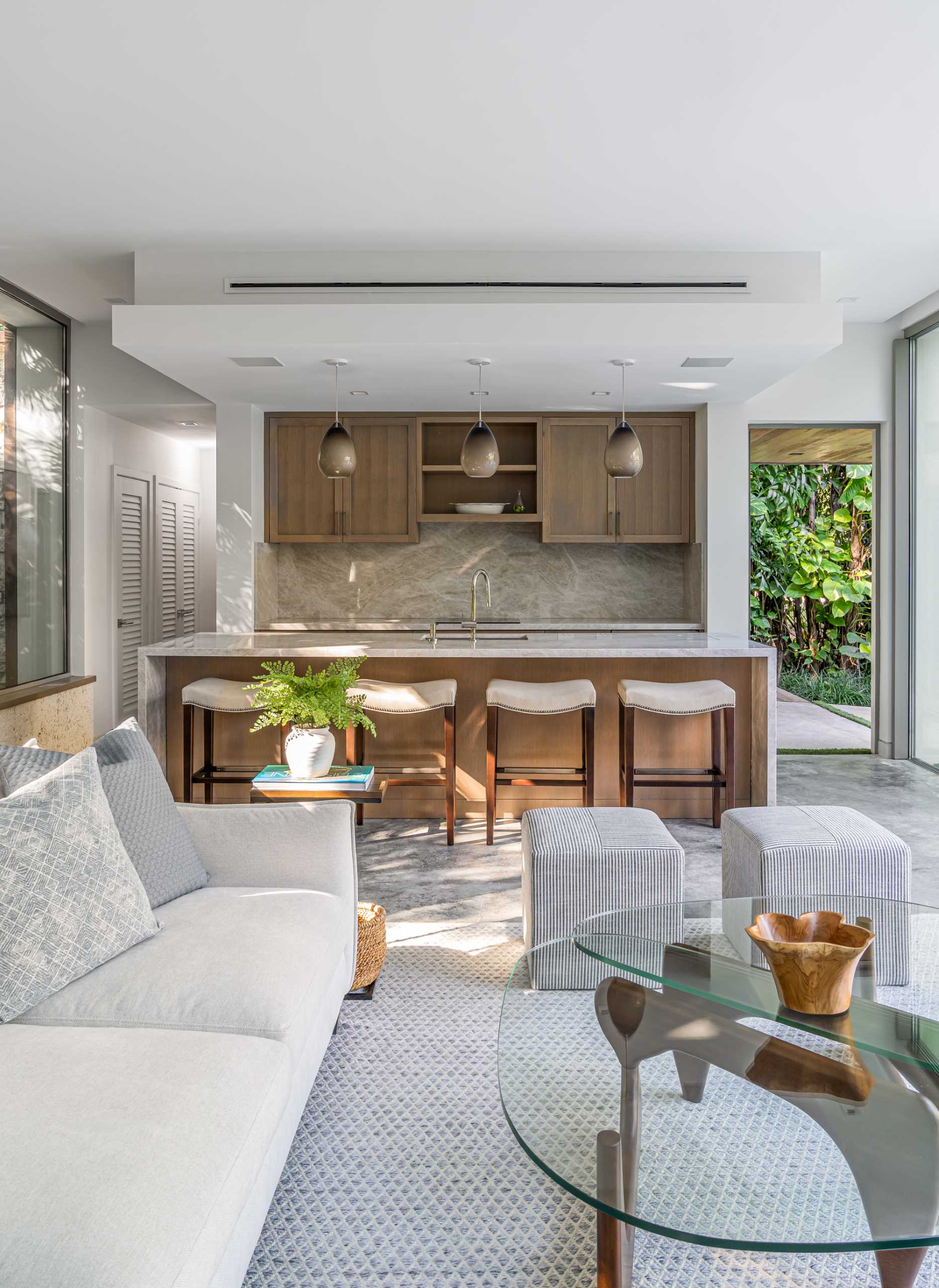 A modern backyard pavilion includes a kitchen with wood cabinetry, an island, and stool seating.