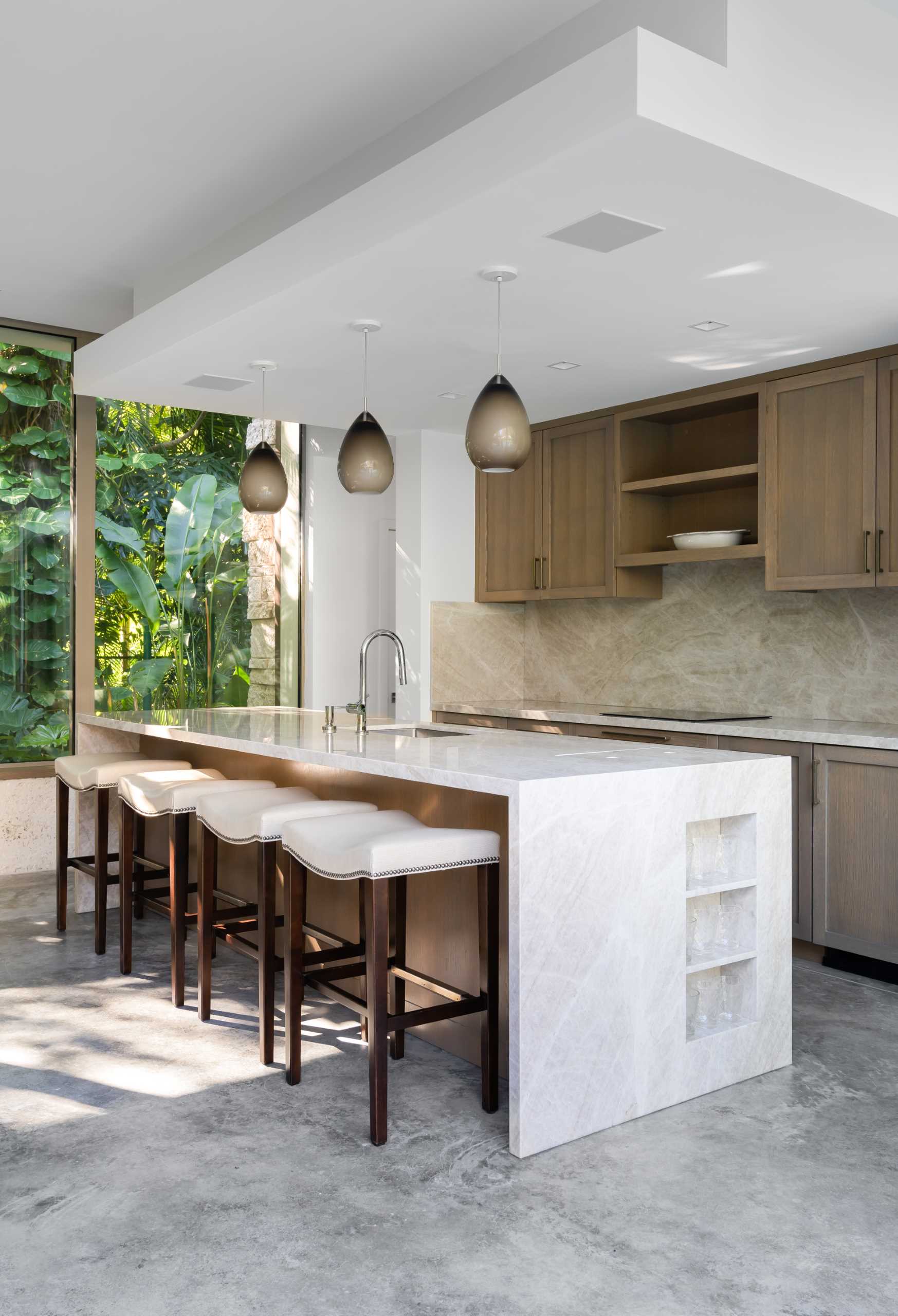 A modern backyard pavilion includes a kitchen with wood cabinetry, an island, and stool seating.