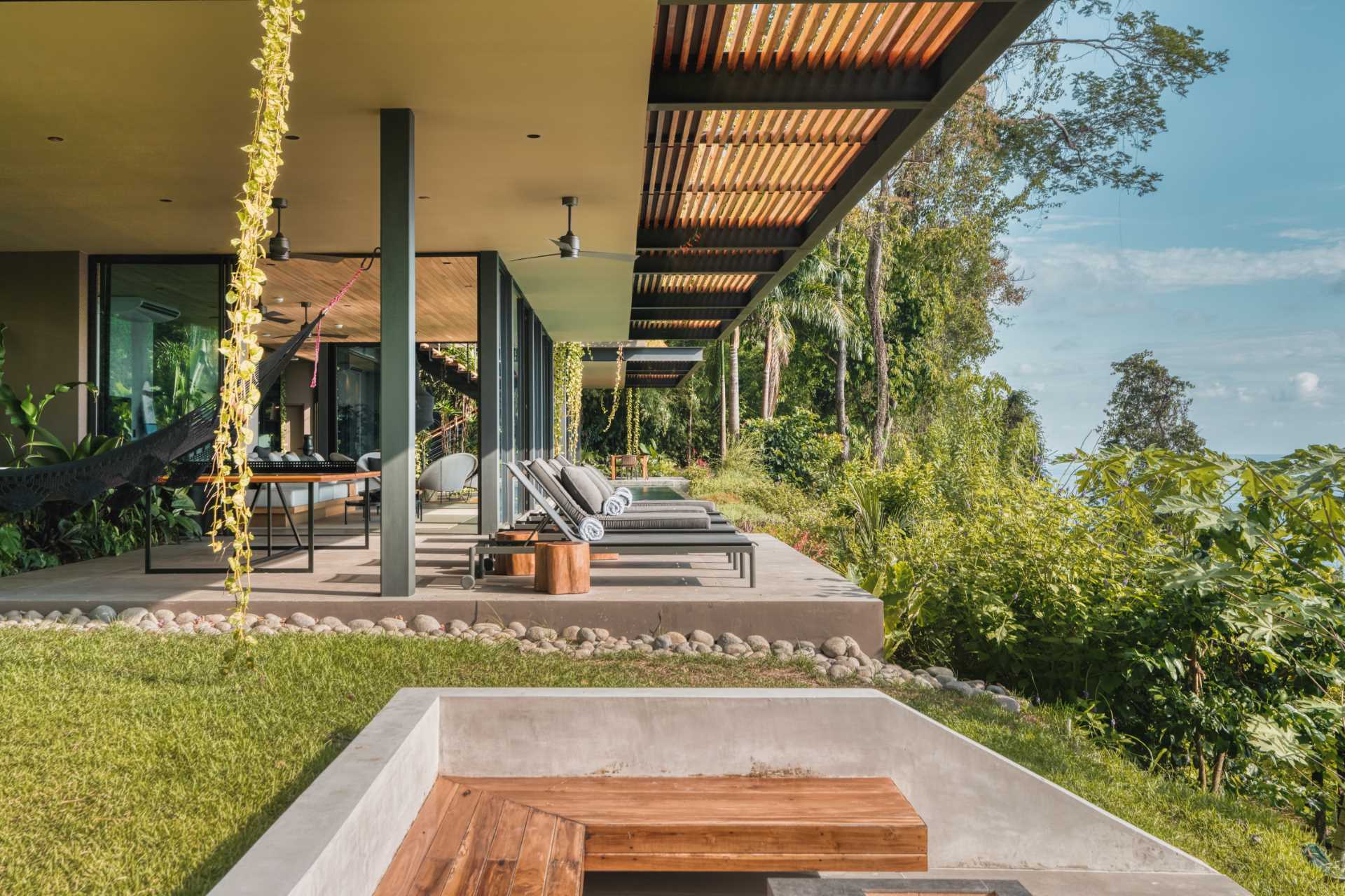 A modern home with outdoor spaces that include a series of sun lounges at one end of the pool and a dining area at the other.